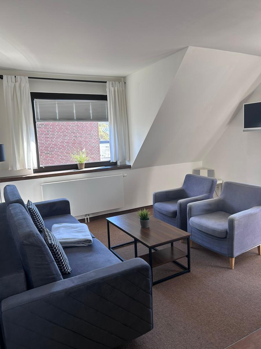 Wohnzimmer mit Sofa, zwei Sesseln, Couchtisch und Fenster mit Blick auf Backsteinmauer.