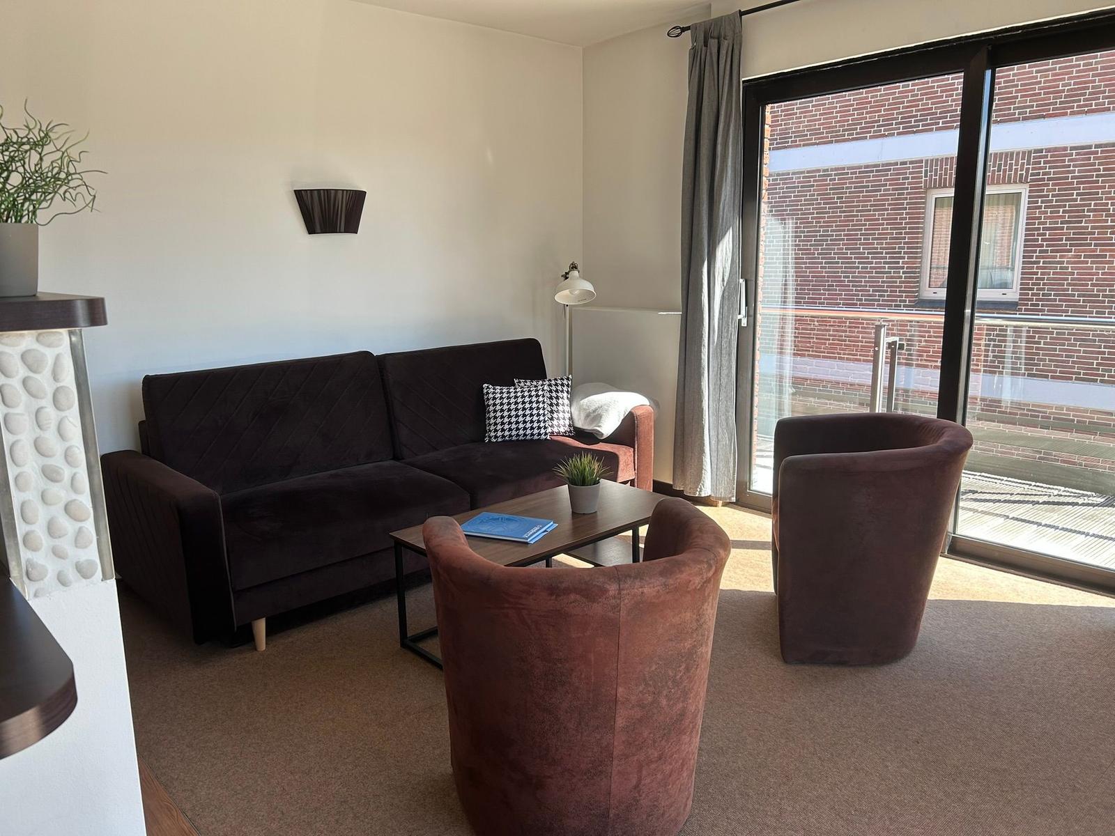 Wohnzimmer mit Sofa, zwei Sesseln und Glasfront zur Terrasse.
