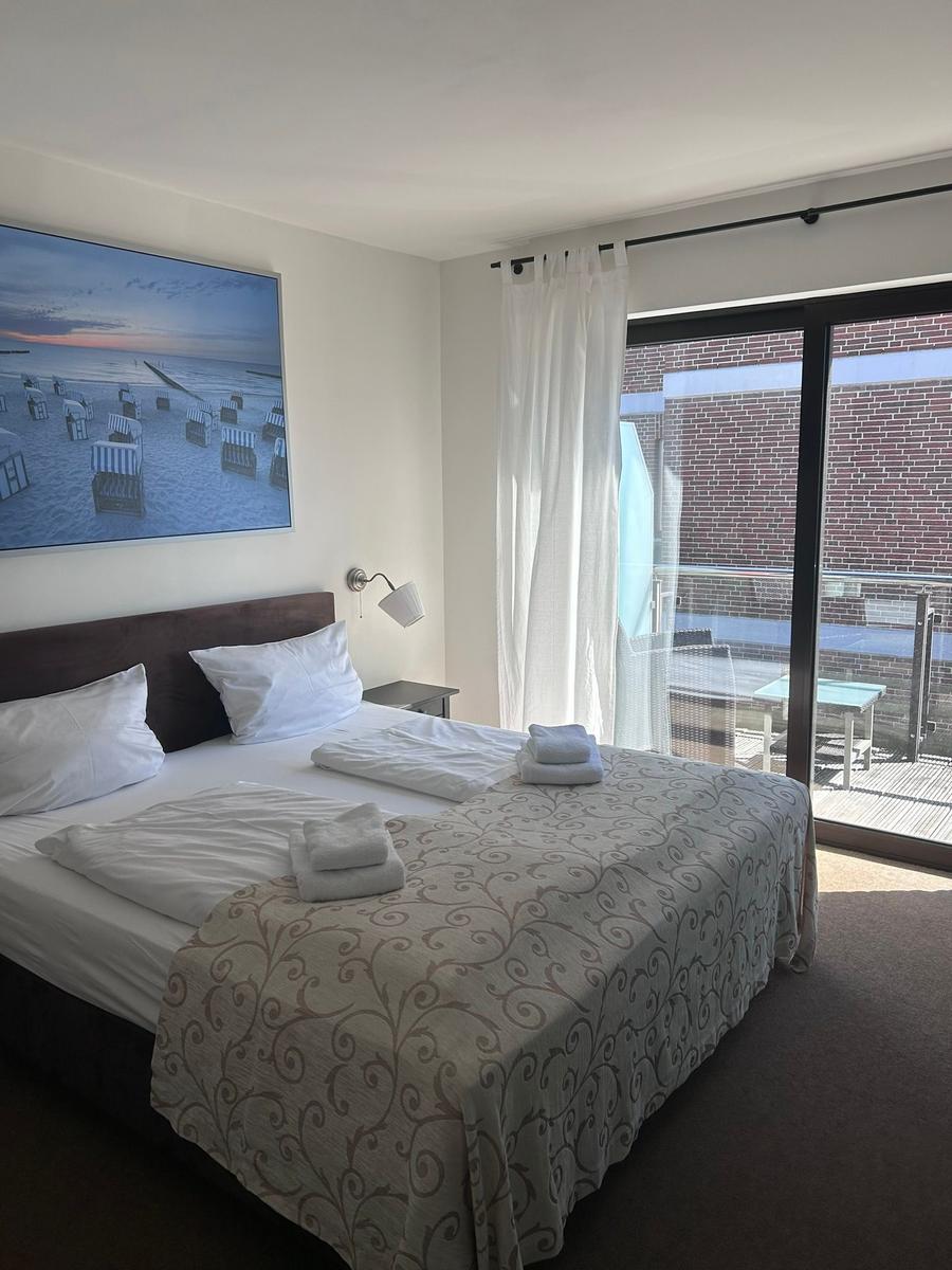 Schlafzimmer mit Doppelbett, Fenster und Balkon. Wandbild zeigt Strand.