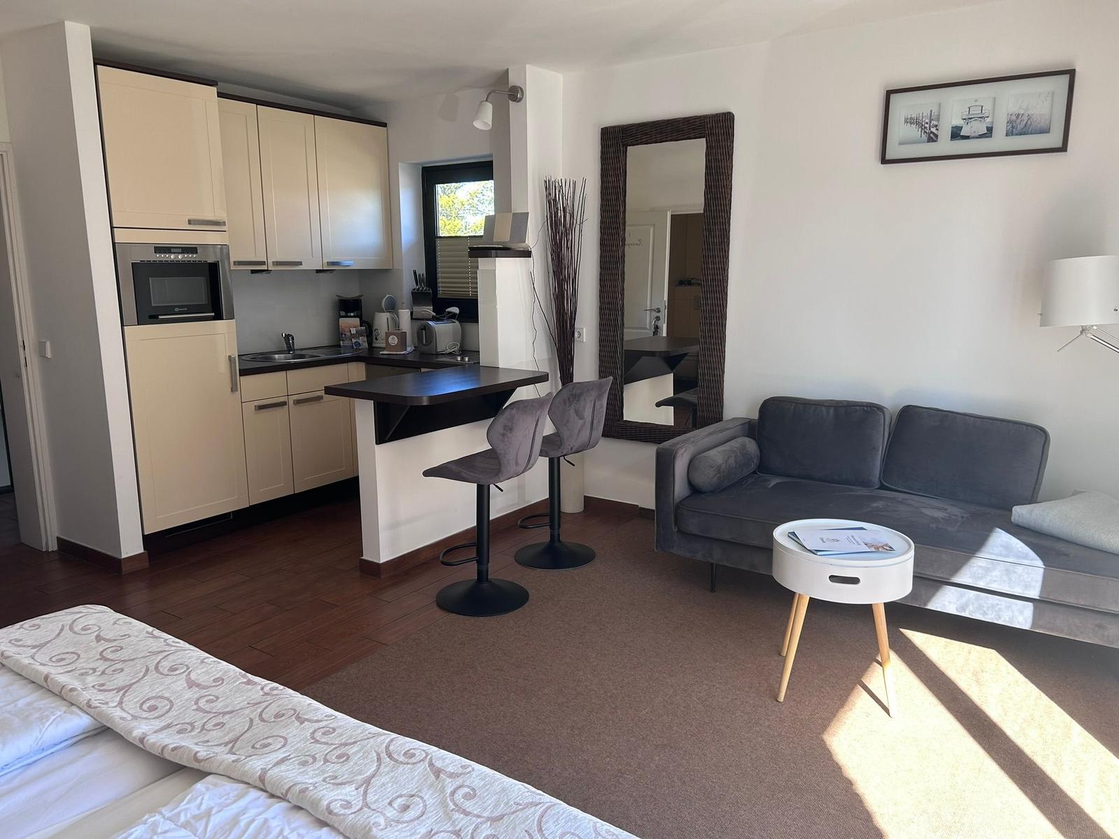 Wohnung mit Küche, Wohnbereich und Bett. Sofa, Tisch und Spiegel sichtbar.