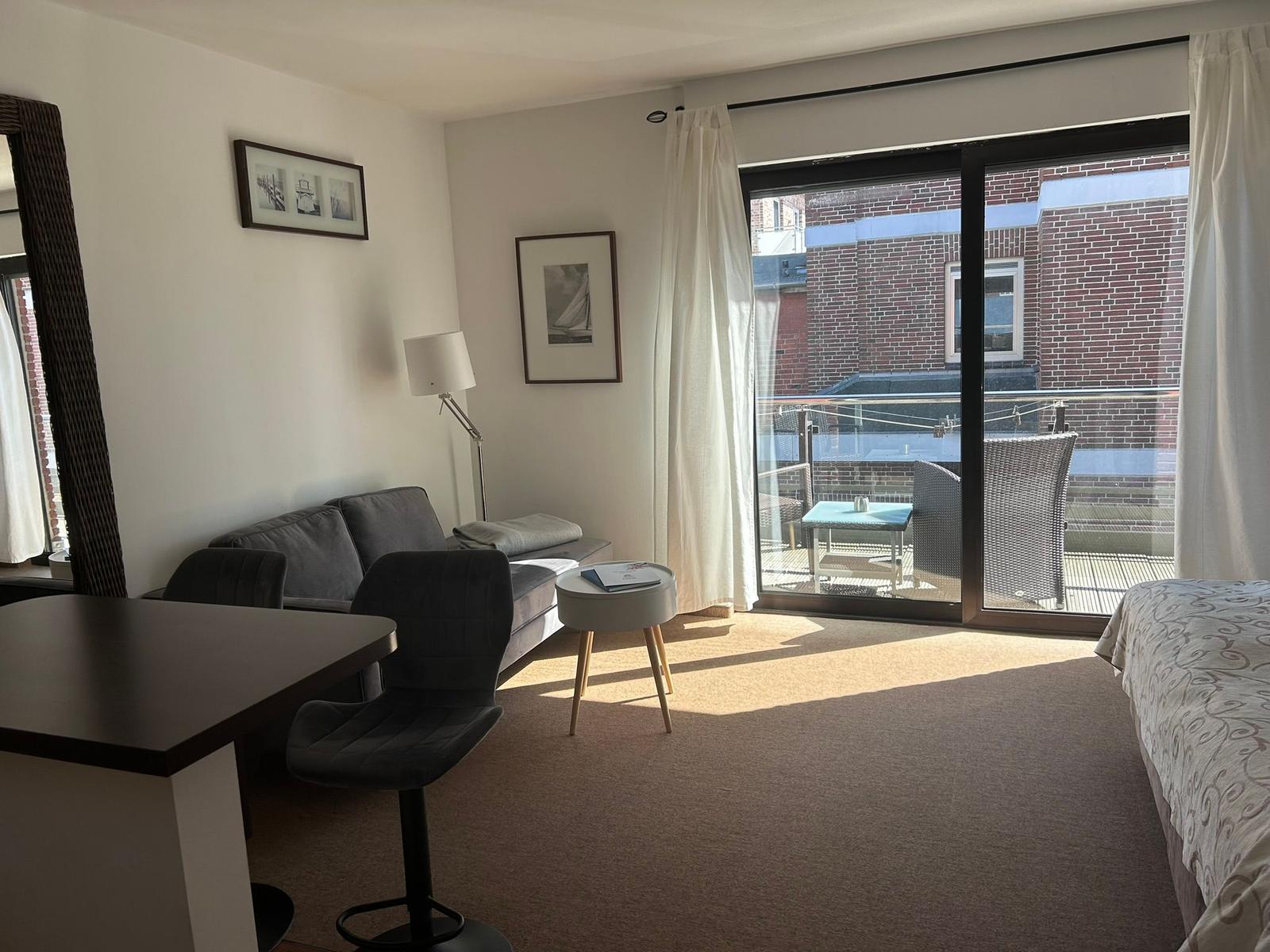 Wohnraum mit Sofa, Tisch und Balkon. Blick auf Backsteinhaus.