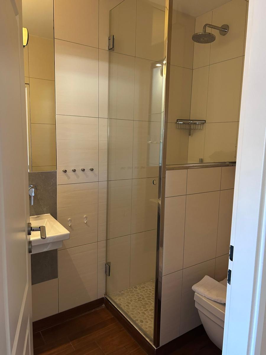 Badezimmer mit Dusche, Waschbecken und Toilette. Fliesenwand und Holzboden.