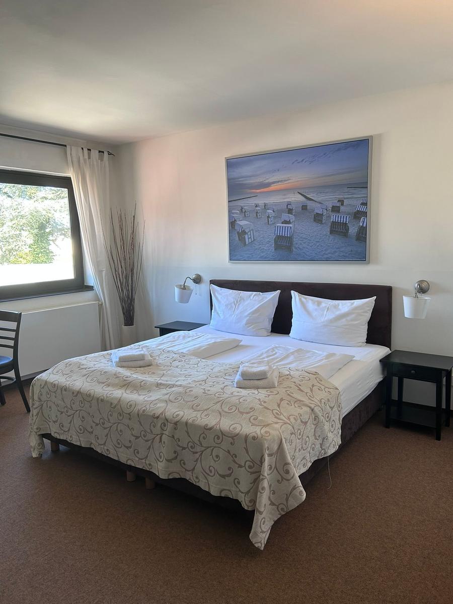 Schlafzimmer mit Bett, Nachttischen und Wandbild. Fenster mit Vorhängen.