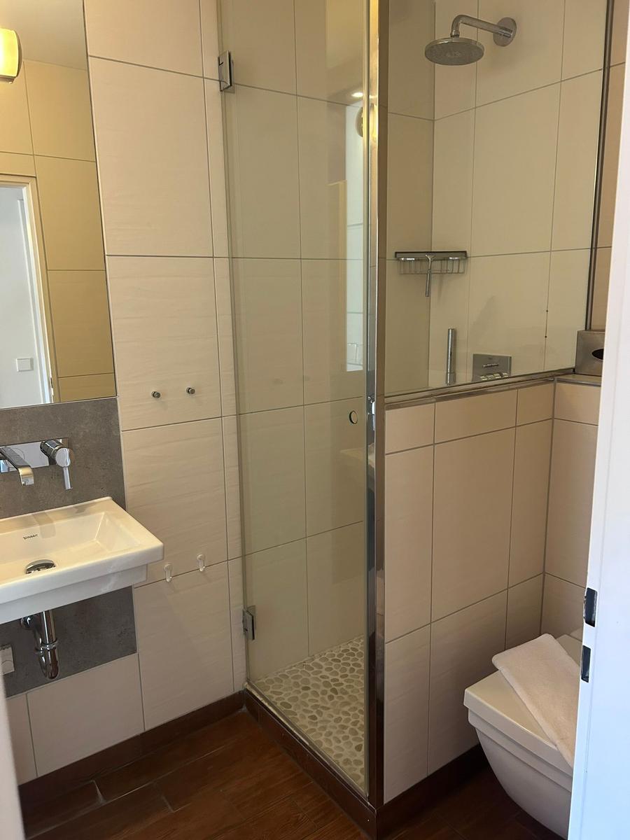 Bad mit Dusche, Waschbecken und Toilette. Fliesenwand und Holzboden.
