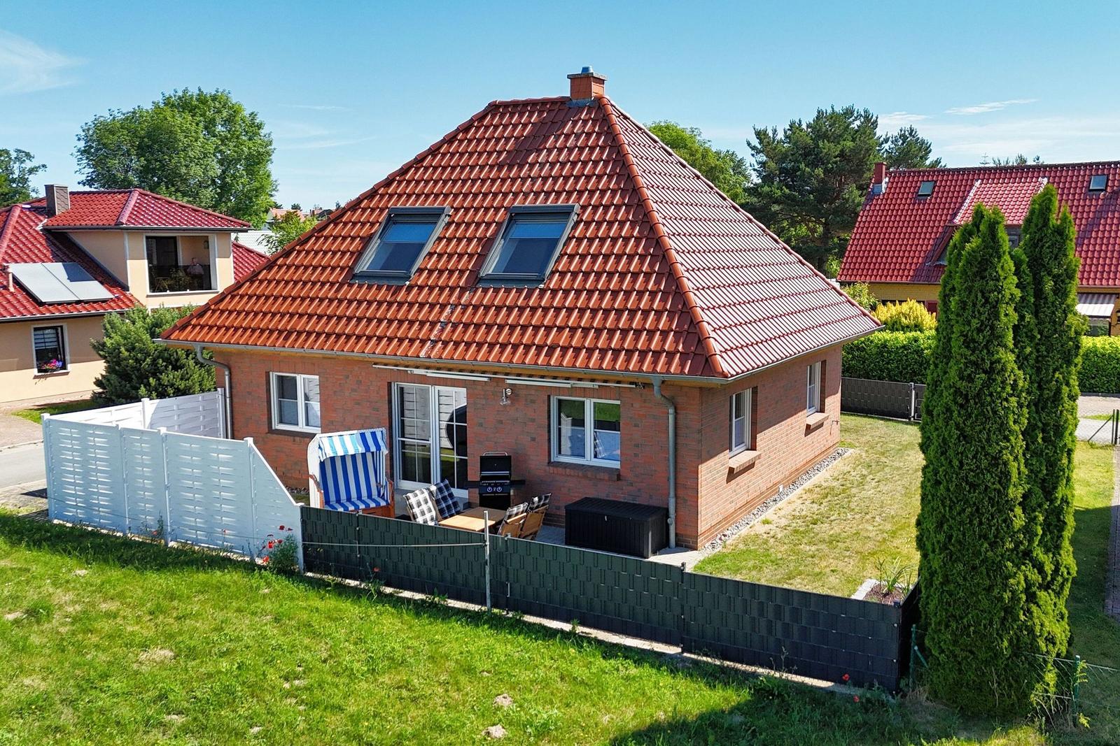 Ein Haus mit rotem Ziegeldach und Garten. Außenterrasse mit Sitzgelegenheit.