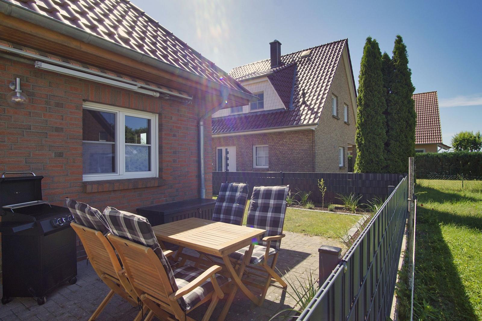 Terrasse mit Holztisch, Stühlen und Grill. Hinterhof mit Rasen und Zaun.