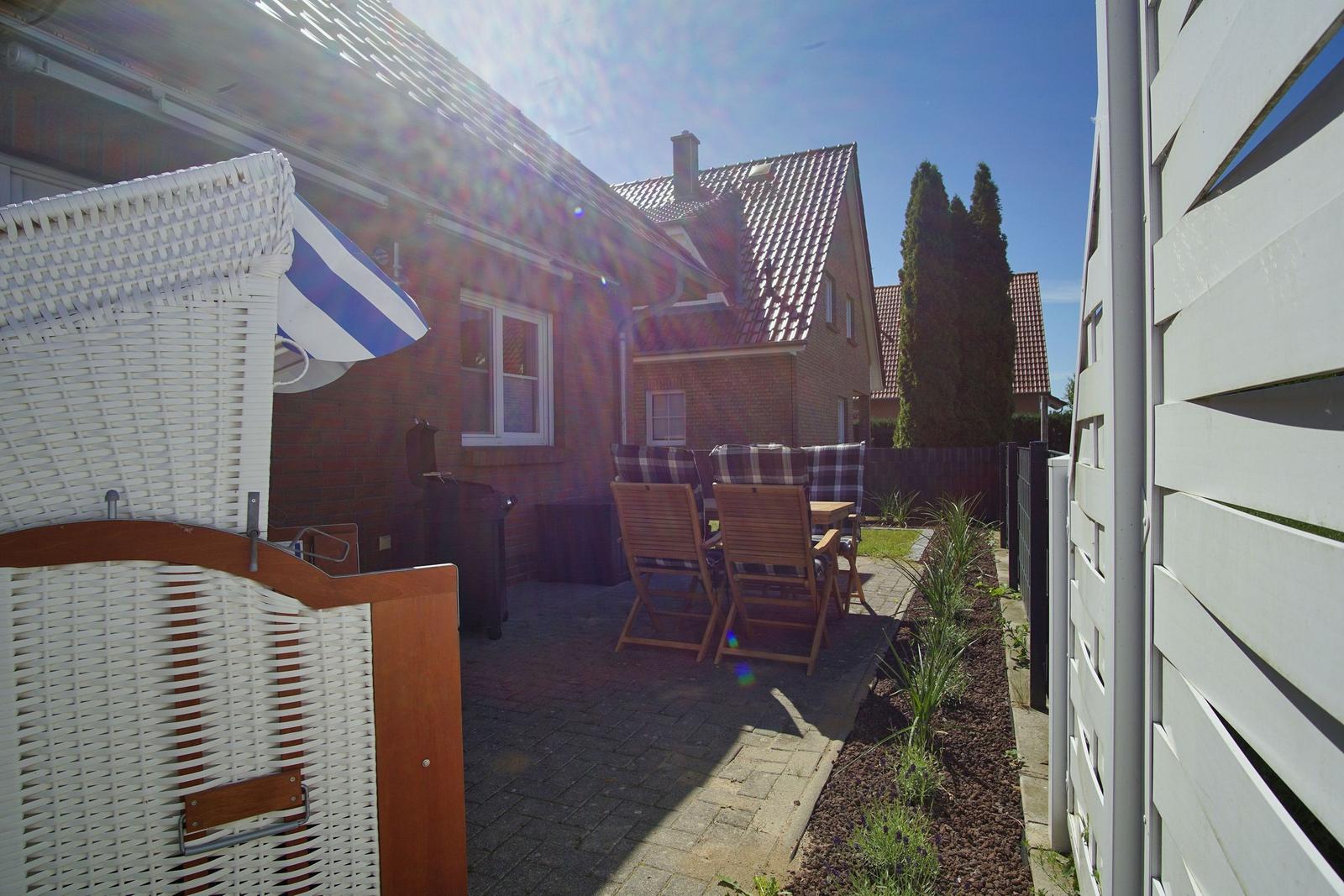 Terrasse mit Holzstühlen und Tisch. Weiße Wicker-Struktur. Hinterhof mit Beete und Zaun.