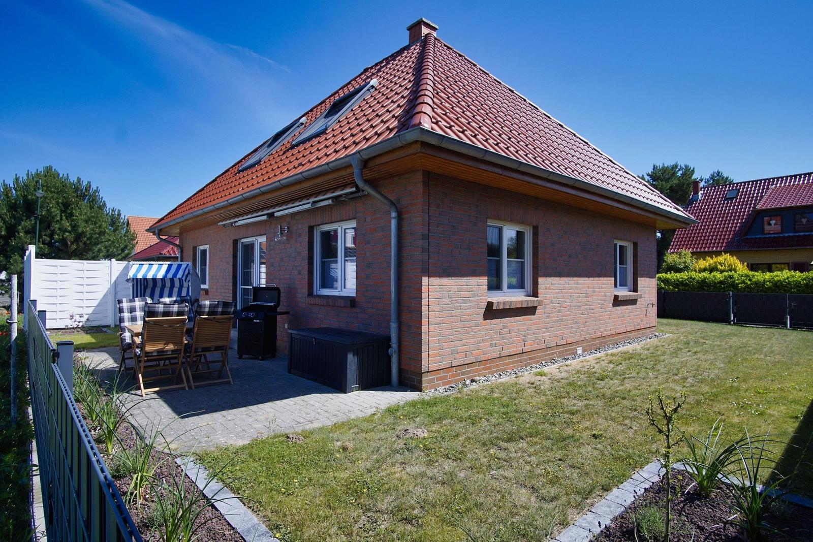 Ein Haus mit rotem Dach und Backsteinfassade. Gartenbereich mit Grill und Sitzgelegenheit.