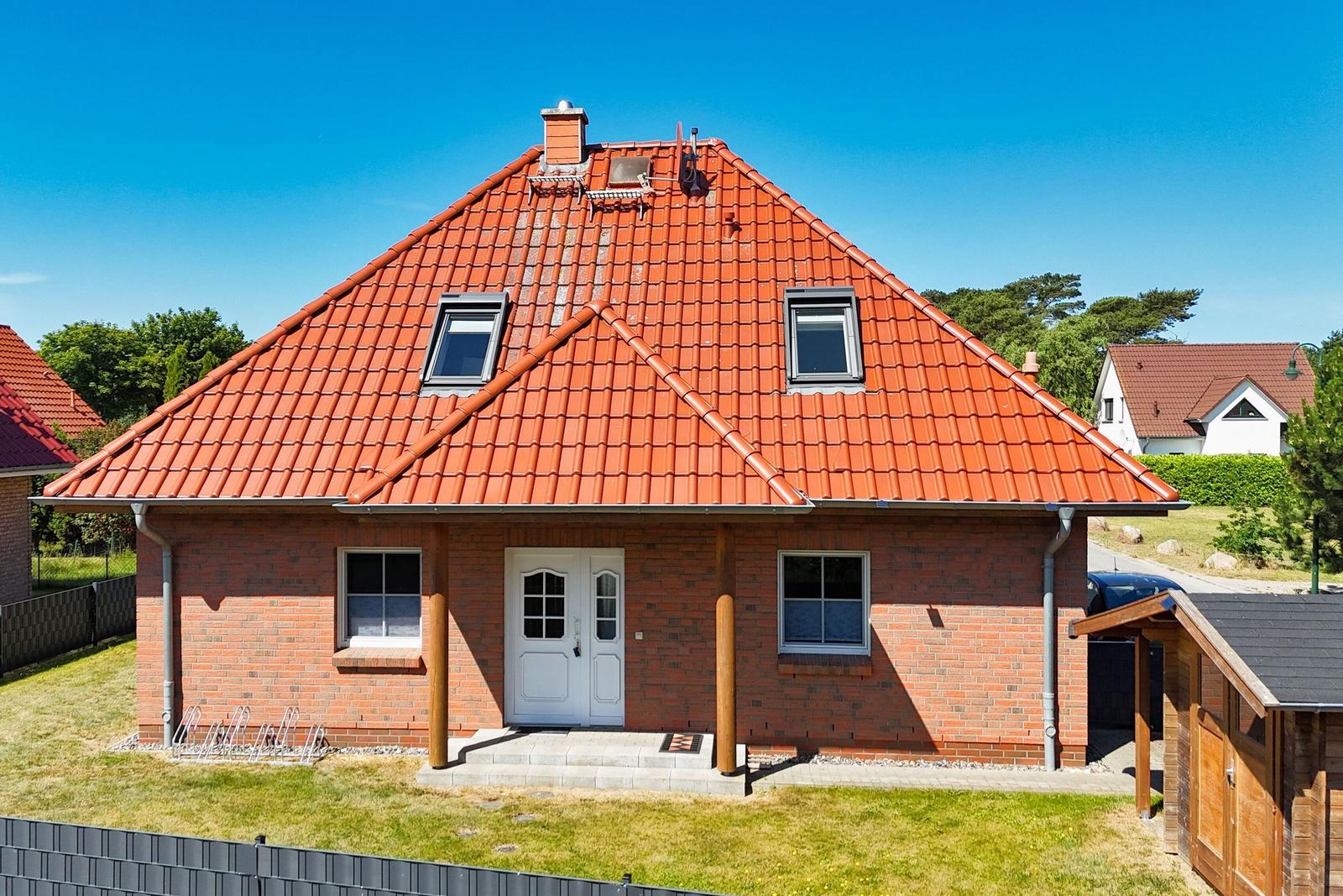 Ein Haus mit rotem Ziegeldach, weißer Tür und grünem Rasen vorne.