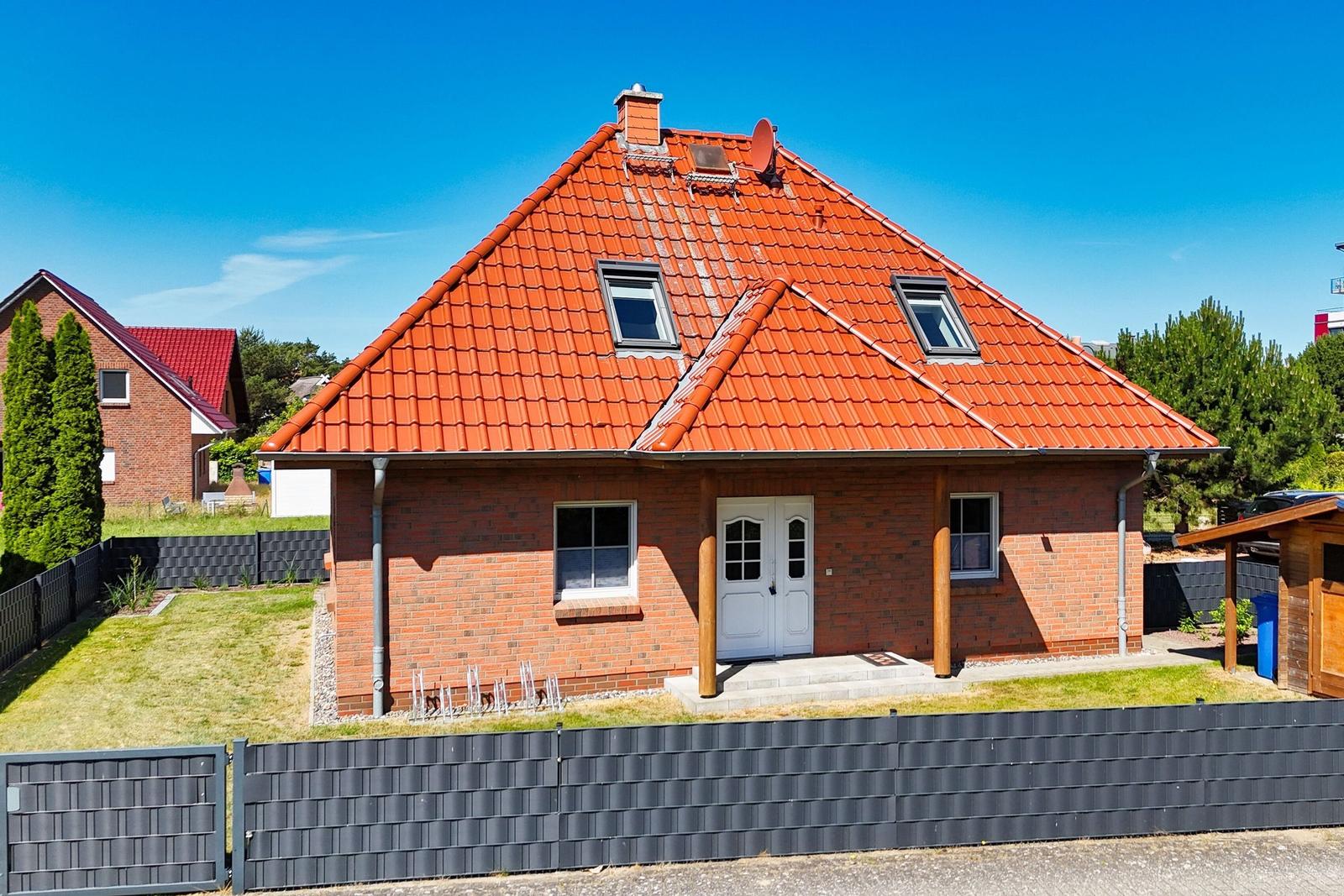Ein Haus mit rotem Dach und Backsteinfassade. Vorderseite mit weißer Tür und Fenstern.