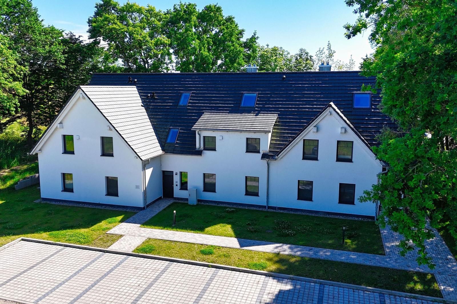 Moderne weiße Villa mit dunklem Dach und grünem Garten.