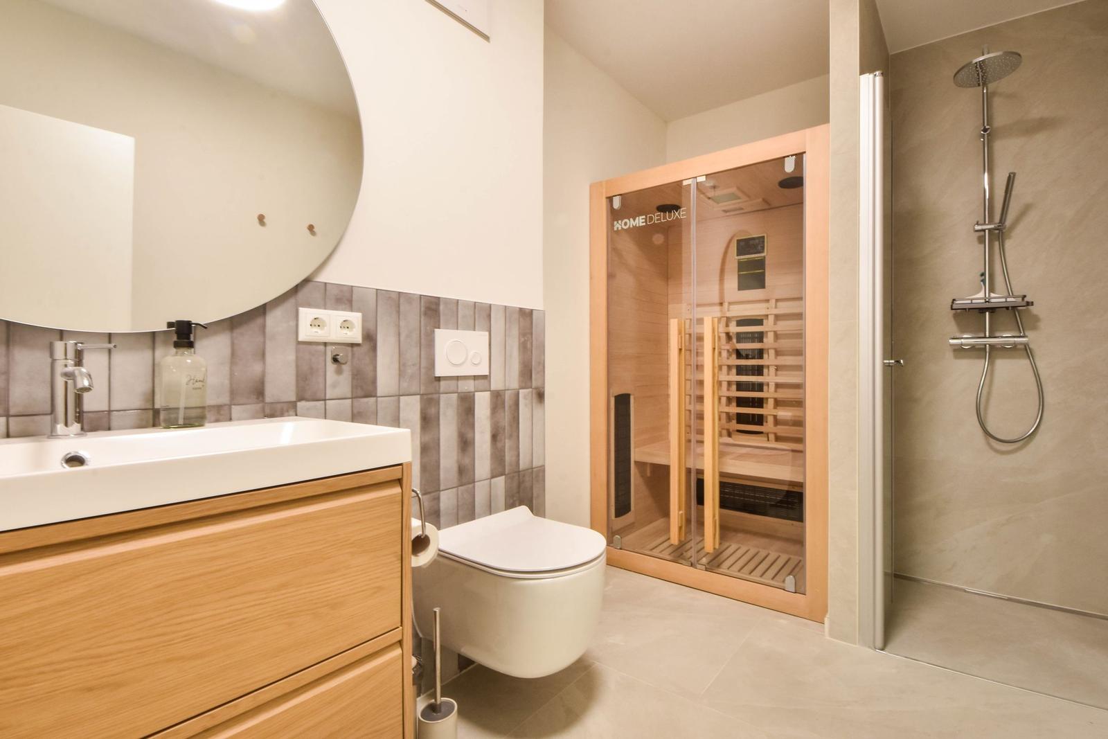 Badezimmer mit Dusche, Sauna und Waschbecken mit Spiegel.