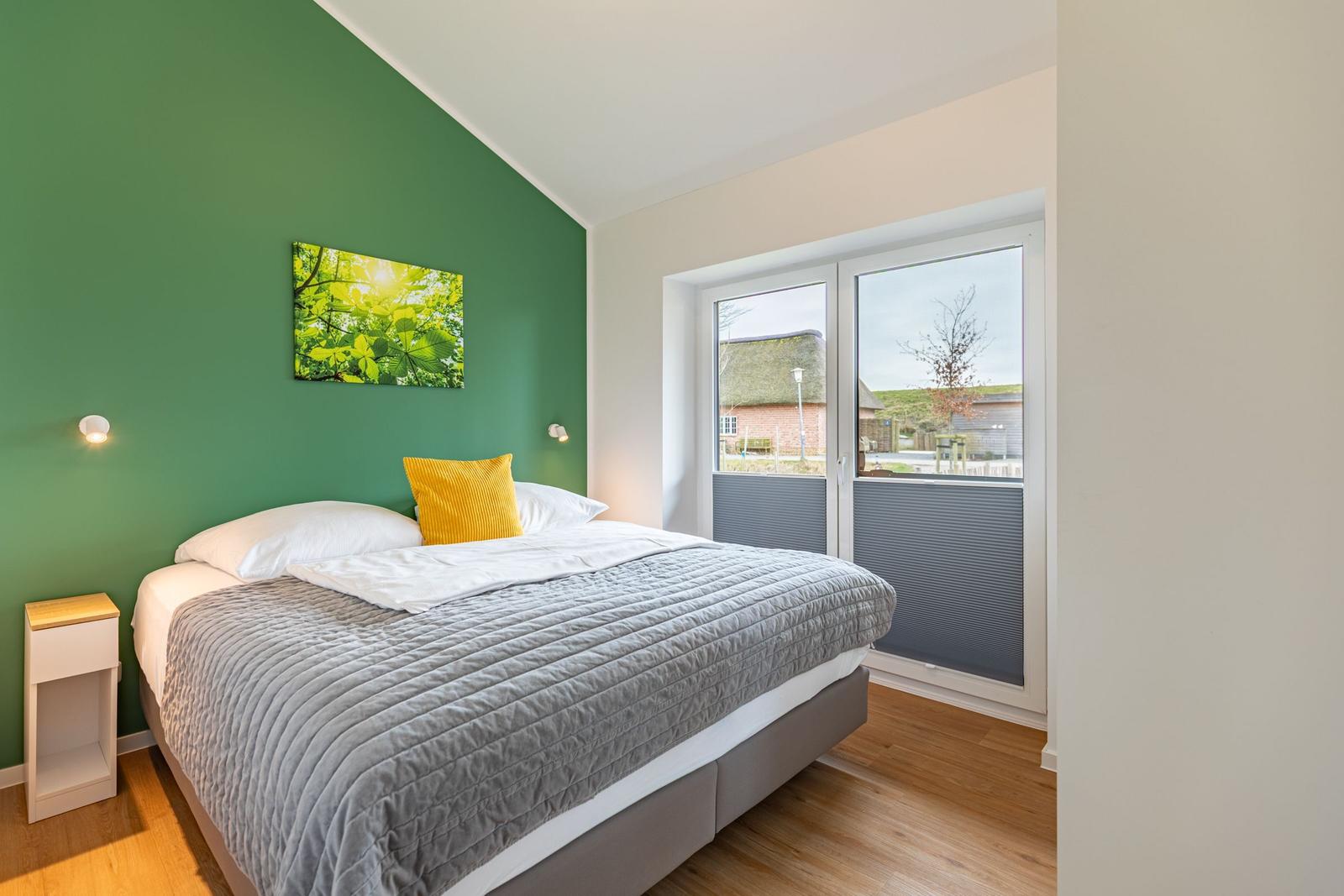 Schlafzimmer mit Bett, grüner Wand und Fenster zur Aussicht.