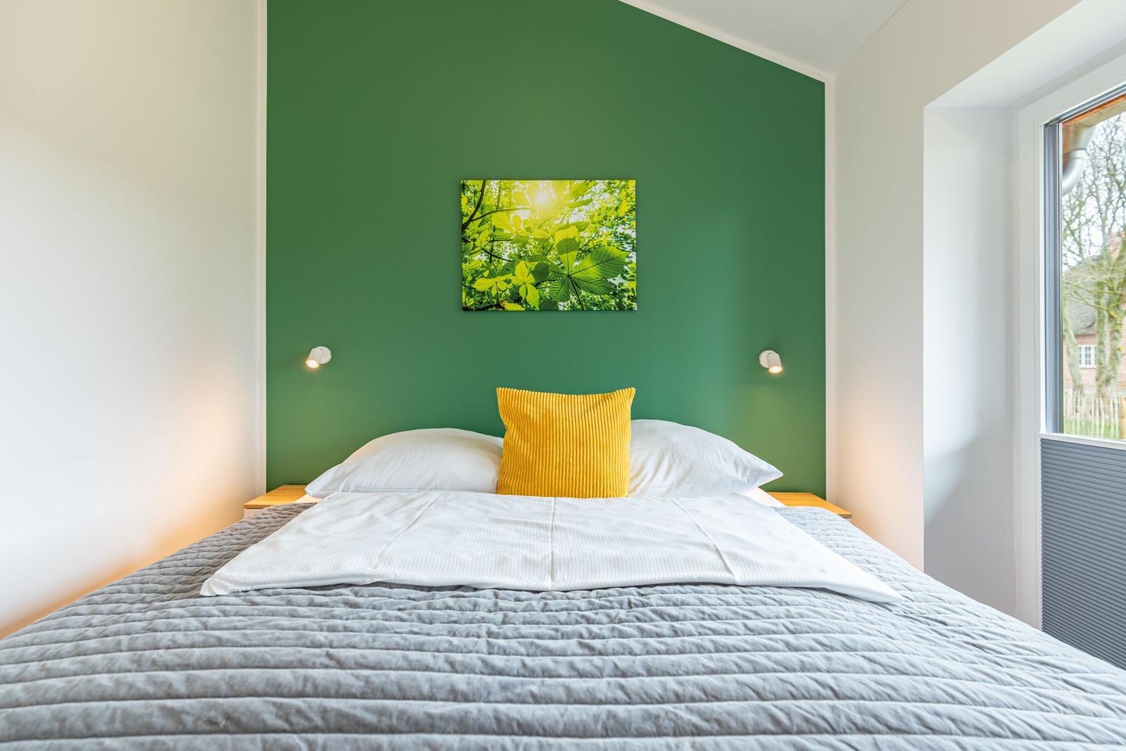 Schlafzimmer mit grüner Wand, Bett mit Kissen und Fenster.