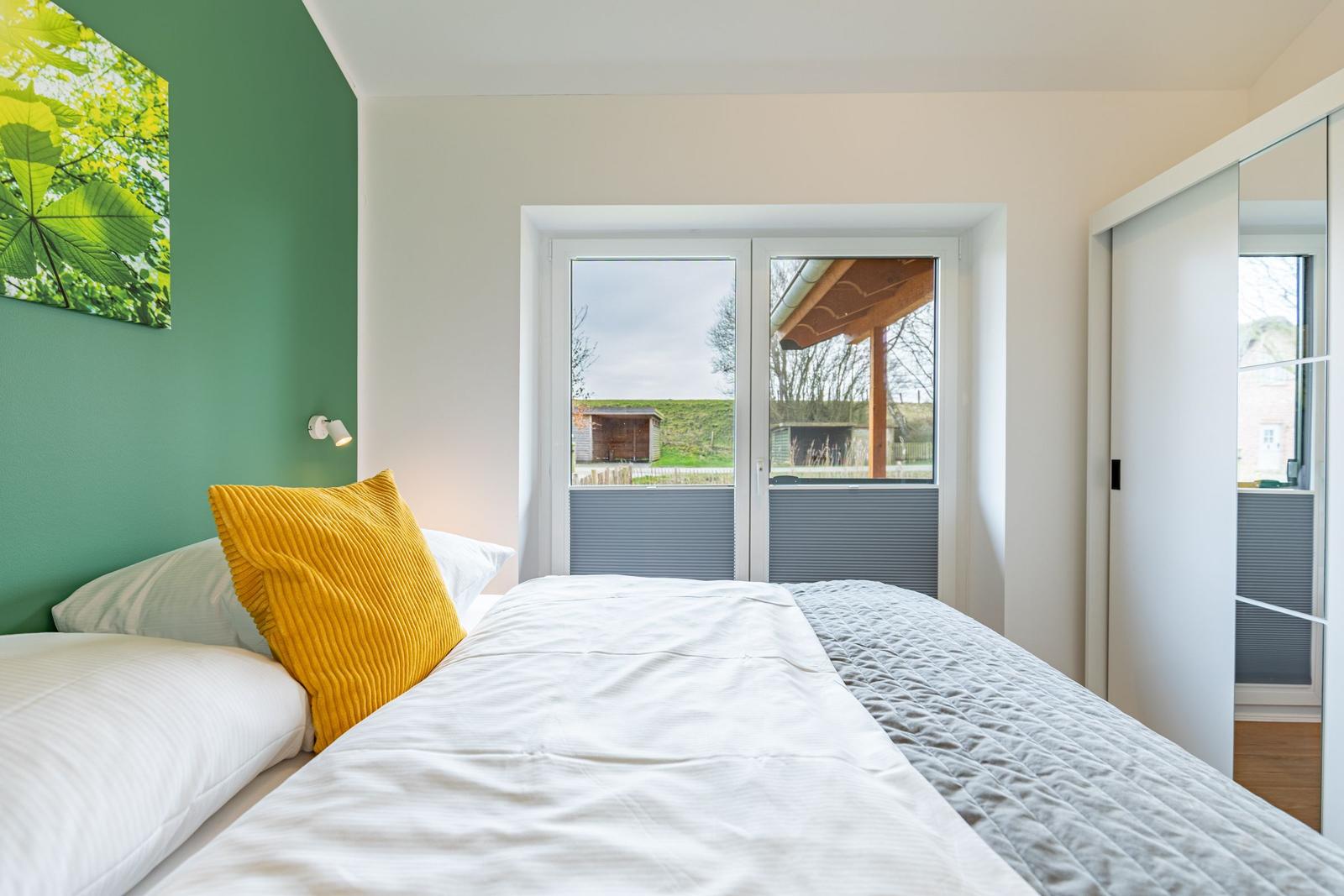 Schlafzimmer mit Bett, gelbem Kissen und Blick auf Außenbereich.