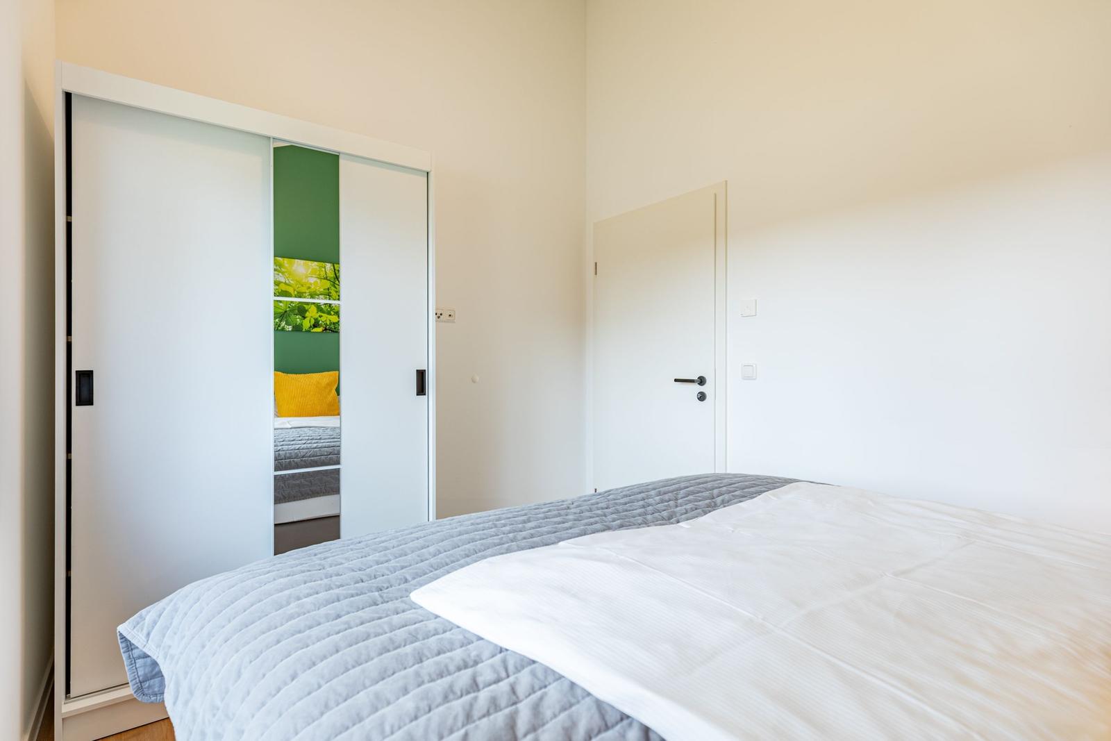 Schlafzimmer mit Bett, Schrank und Tür. Durchgehender Schrank mit Glasfront.