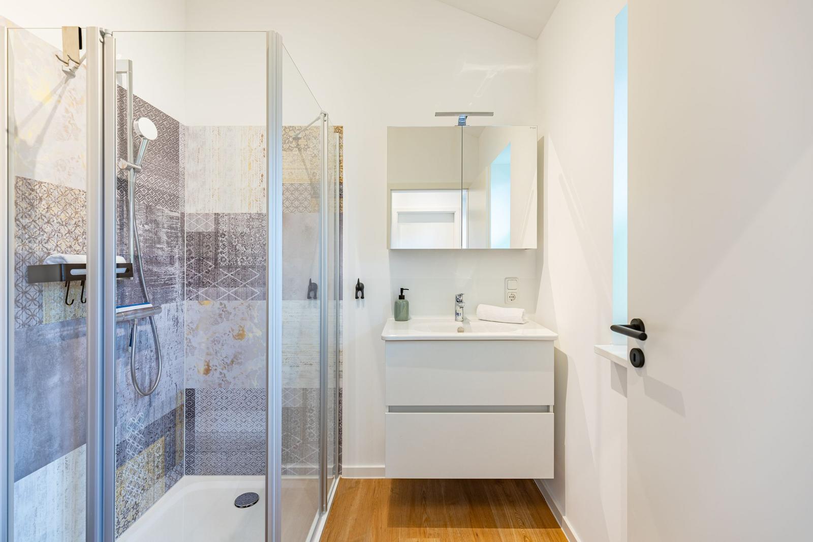 Dusche mit Glaswand, Waschbecken und Spiegelschrank in moderner Badezimmerausstattung.