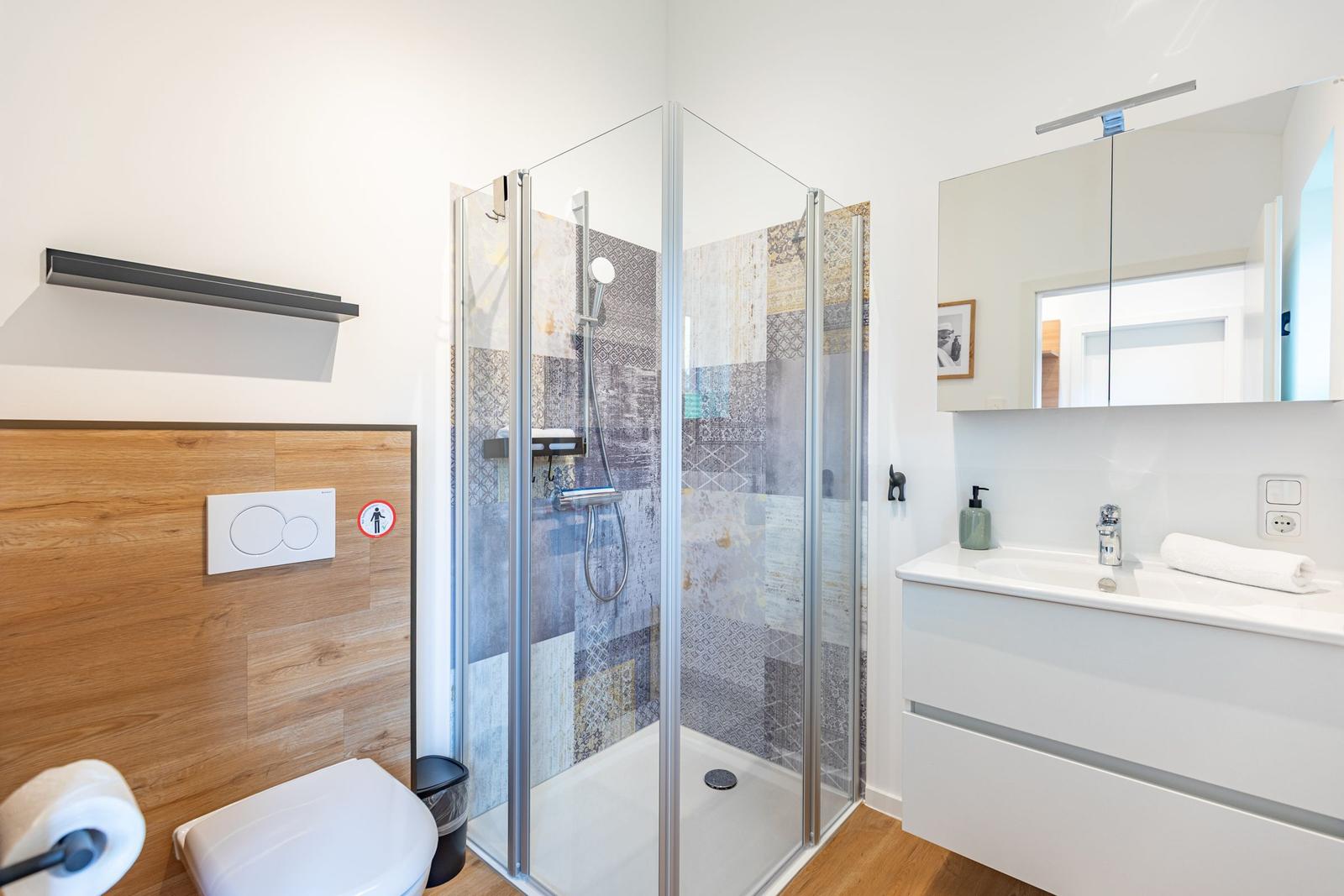 Badezimmer mit Dusche, Waschbecken und Toilette. Fliesenwand und Holzwand.