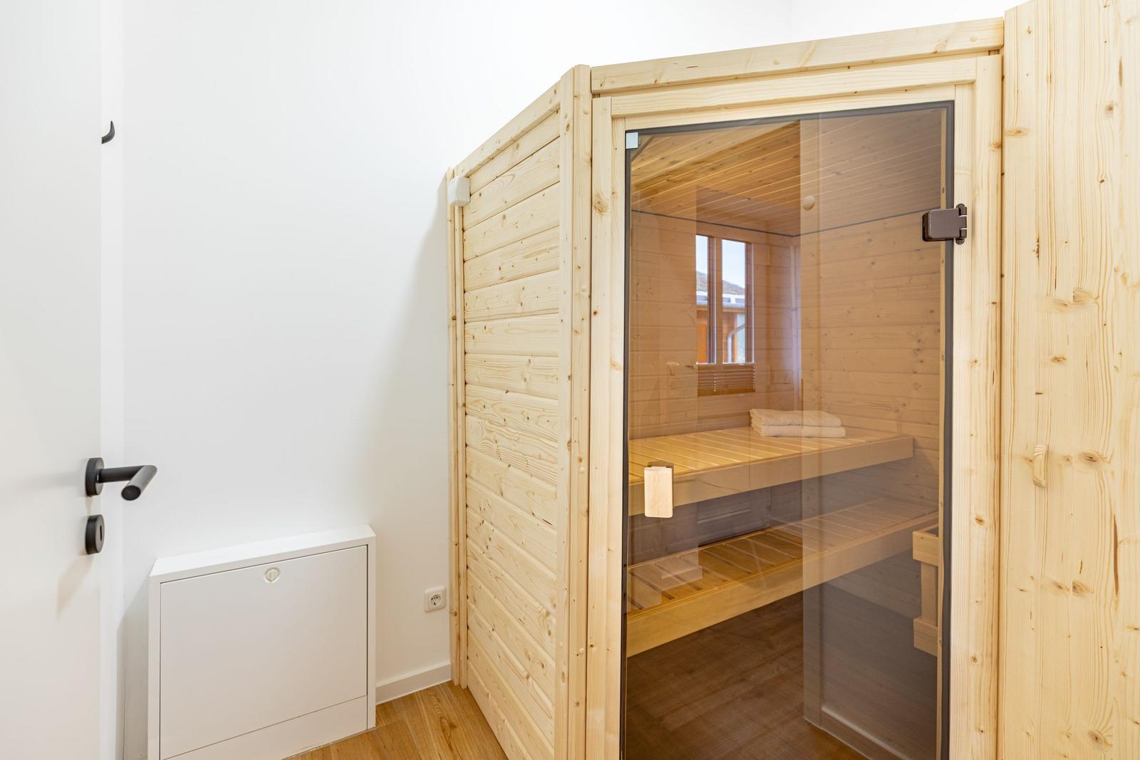 Holzsauna mit Sitzbank und Fenster. Tür und Wand aus Holz. Weiße Wand und Boden.