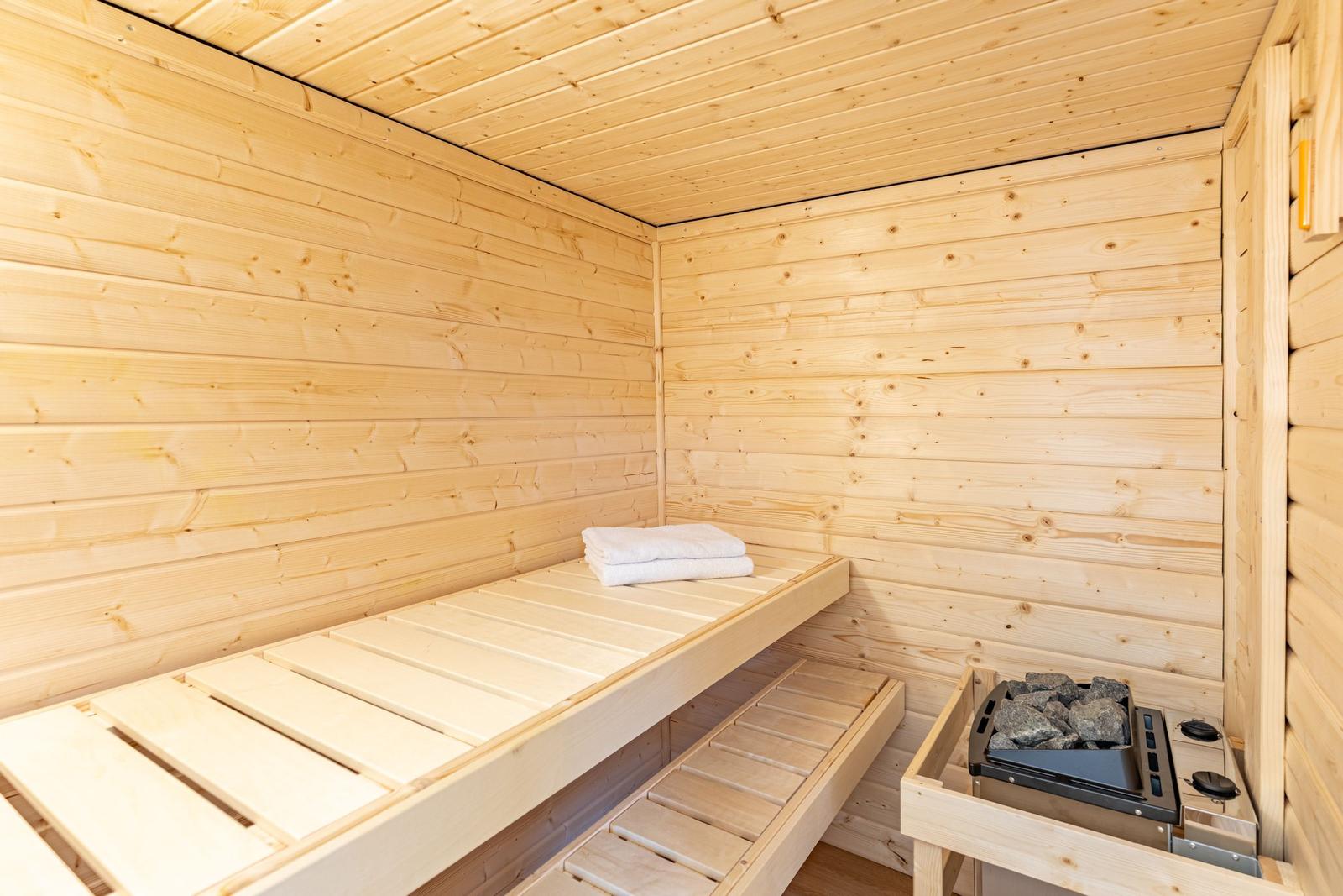 Holzsauna mit Sitzbänken und Heizung. Weiße Handtücher liegen bereit.