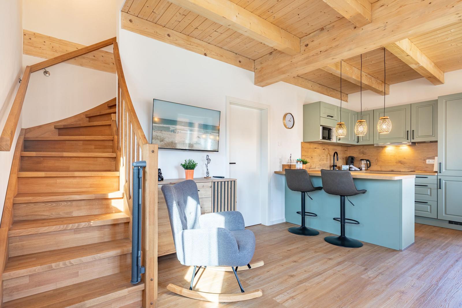 Wohnbereich mit Holztreppe, Kücheninsel und Fernseher an der Wand.