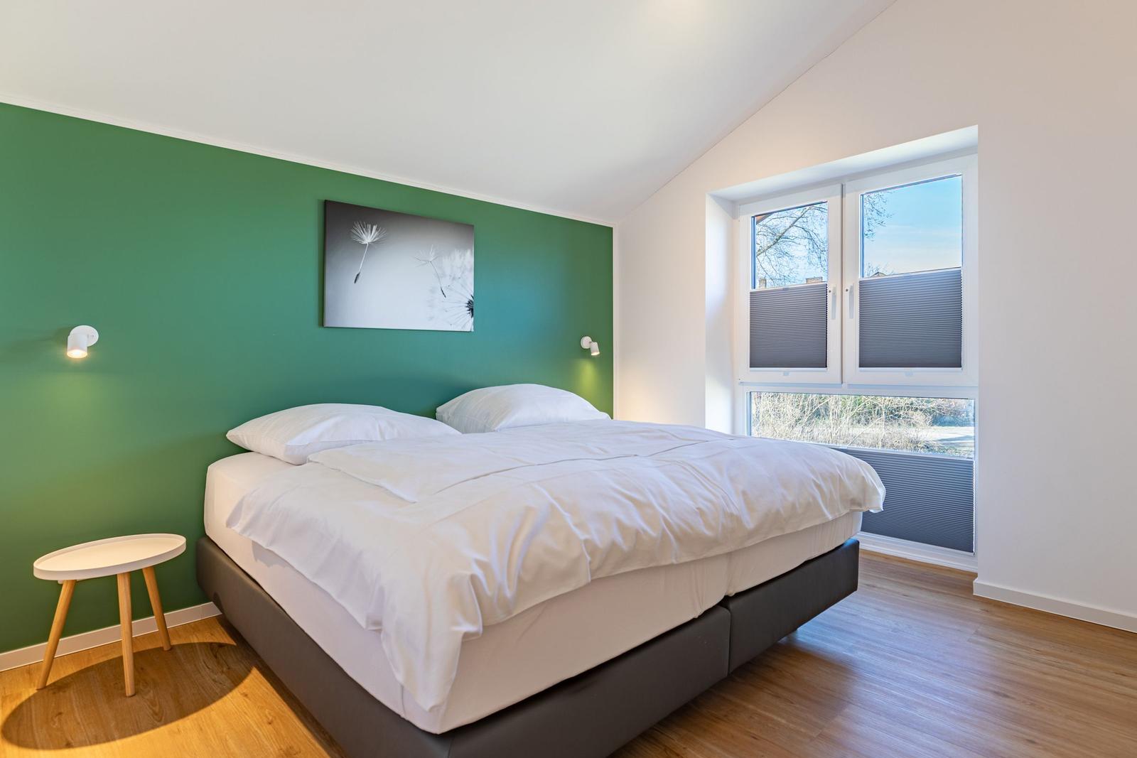 Schlafzimmer mit Doppelbett, grüner Wand und Fenster mit Blick nach draußen.