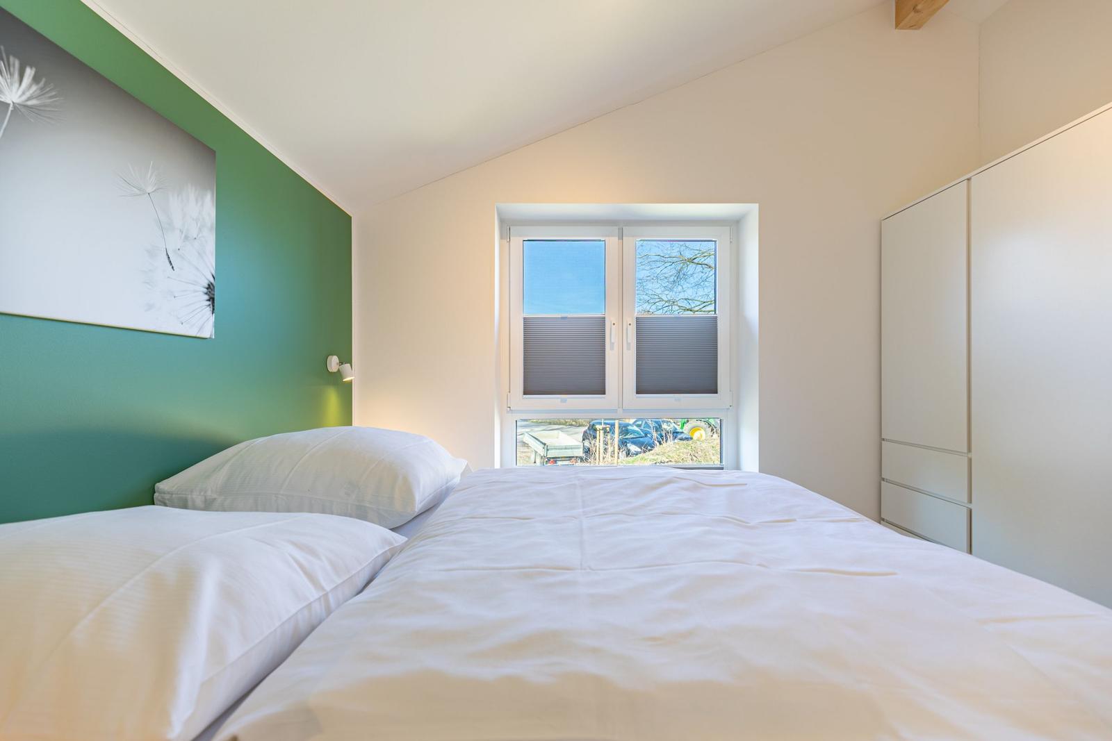 Schlafzimmer mit Bett, Fenster und Kleiderschrank. Wand mit Bild und grünem Farbton.