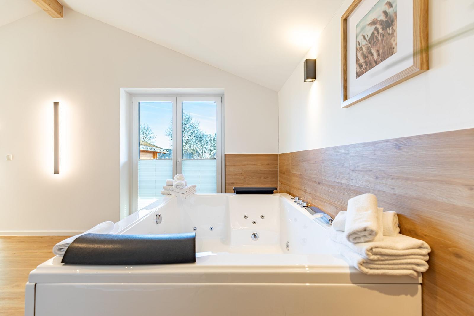 Eine Whirlpool-Badewanne mit Blick auf Außenbereich. Holzwand und Fenster sichtbar.