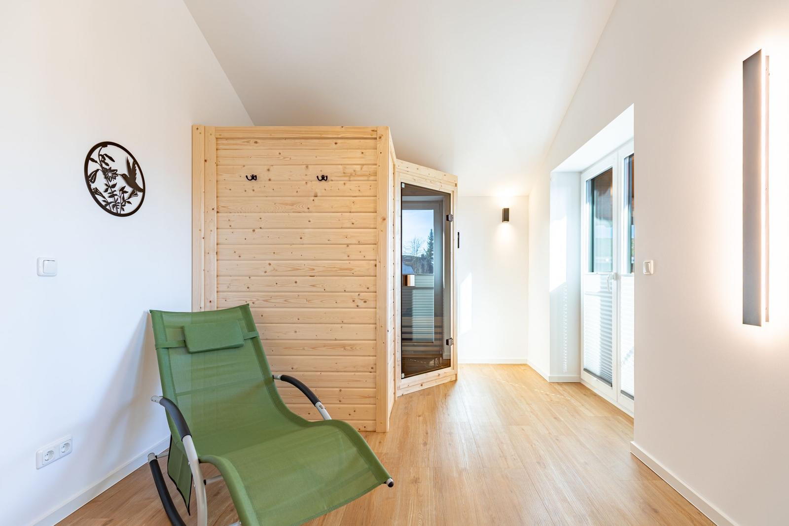 Ein Raum mit Holzfußboden, grüner Liege und Holzsauna mit Glasfront.