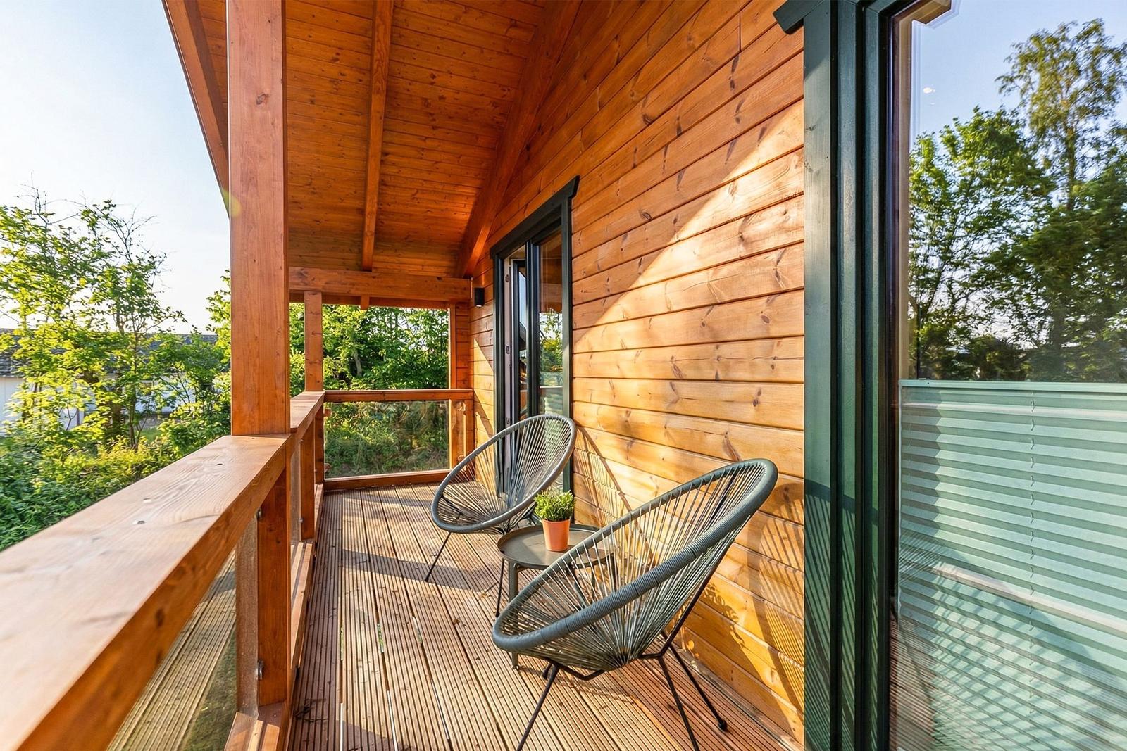 Holzveranda mit zwei Stühlen und Tisch. Blick auf grüne Bäume. Glasfront und Holzwände.