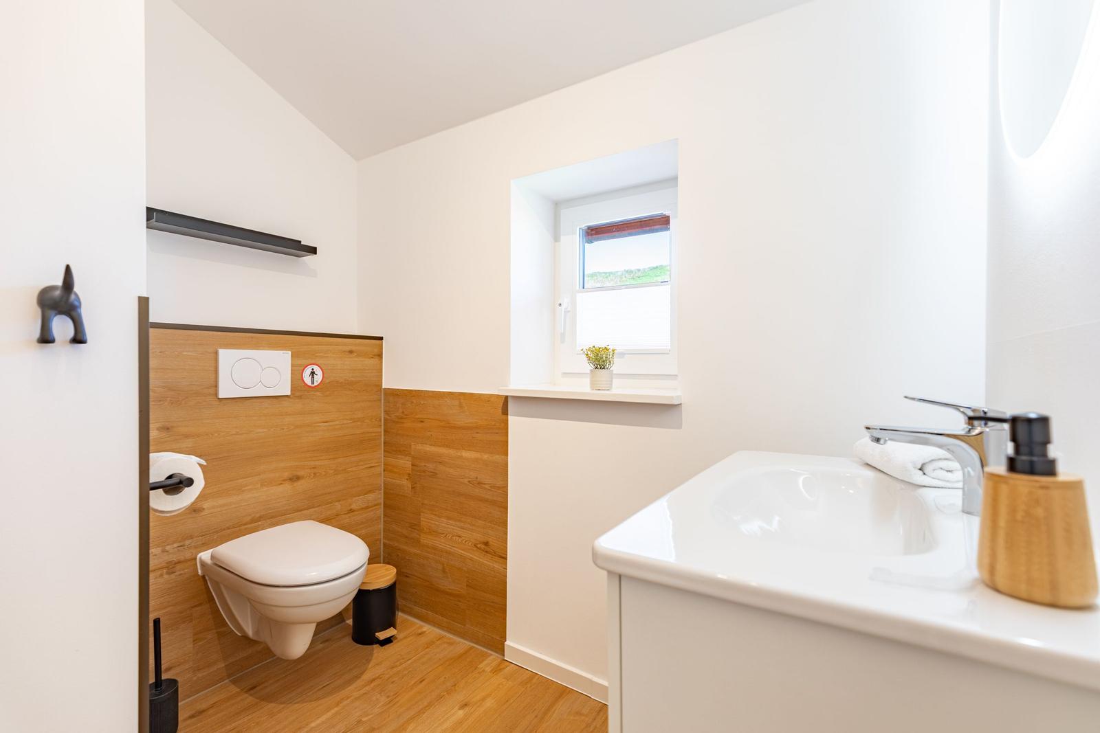 Sanitärkabinett mit Toilette, Waschbecken und kleinem Fenster mit Pflanze.