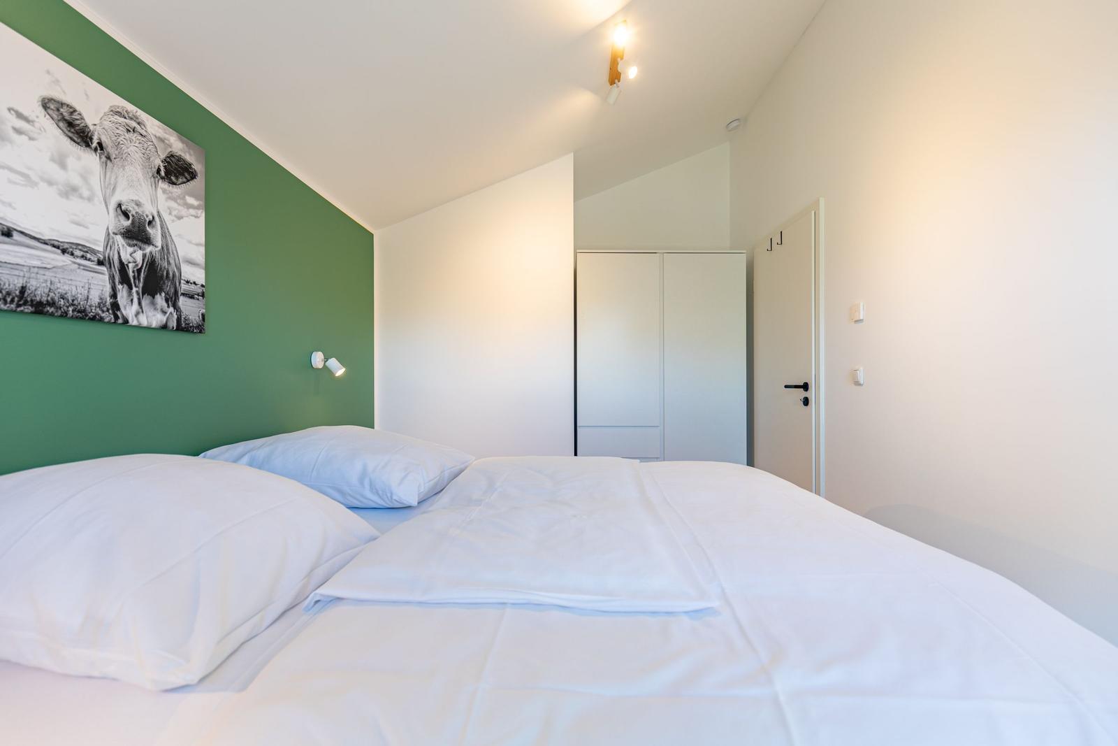 Schlafzimmer mit Bett, grüner Wand und Wandbild einer Kuh.
