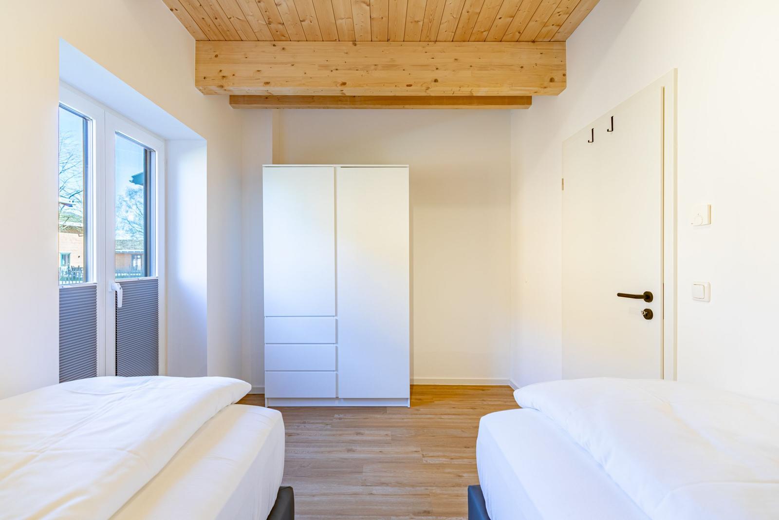 Zwei Betten, weißer Schrank, Holzdecke und Fenster mit Blick.