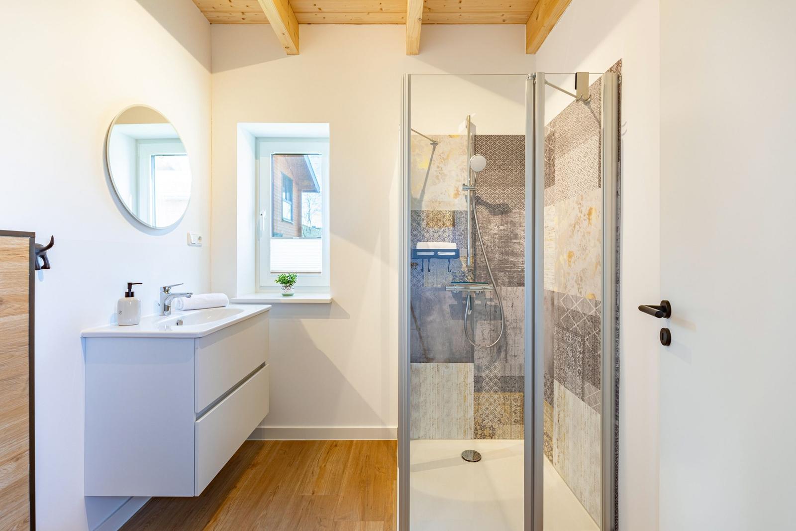 Badezimmer mit Dusche, Waschbecken und Fenster.