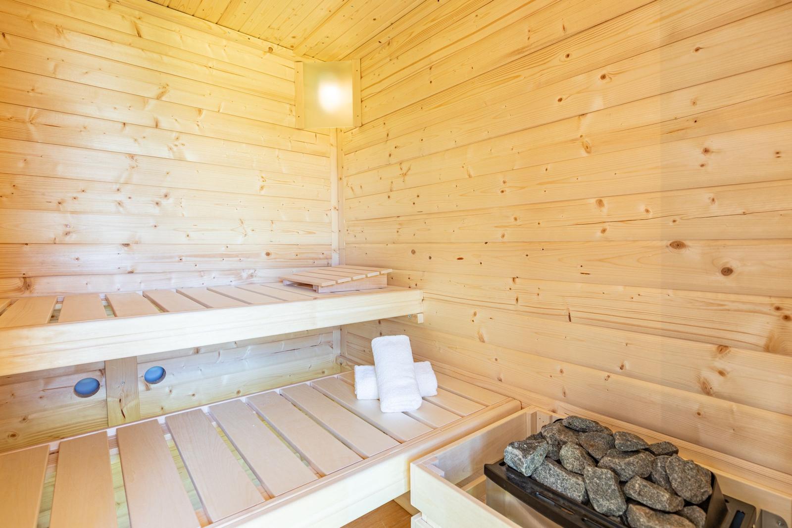 Sauna mit Holzwand, Sitzbänken und Steinblock. Weiße Handtücher liegen bereit.