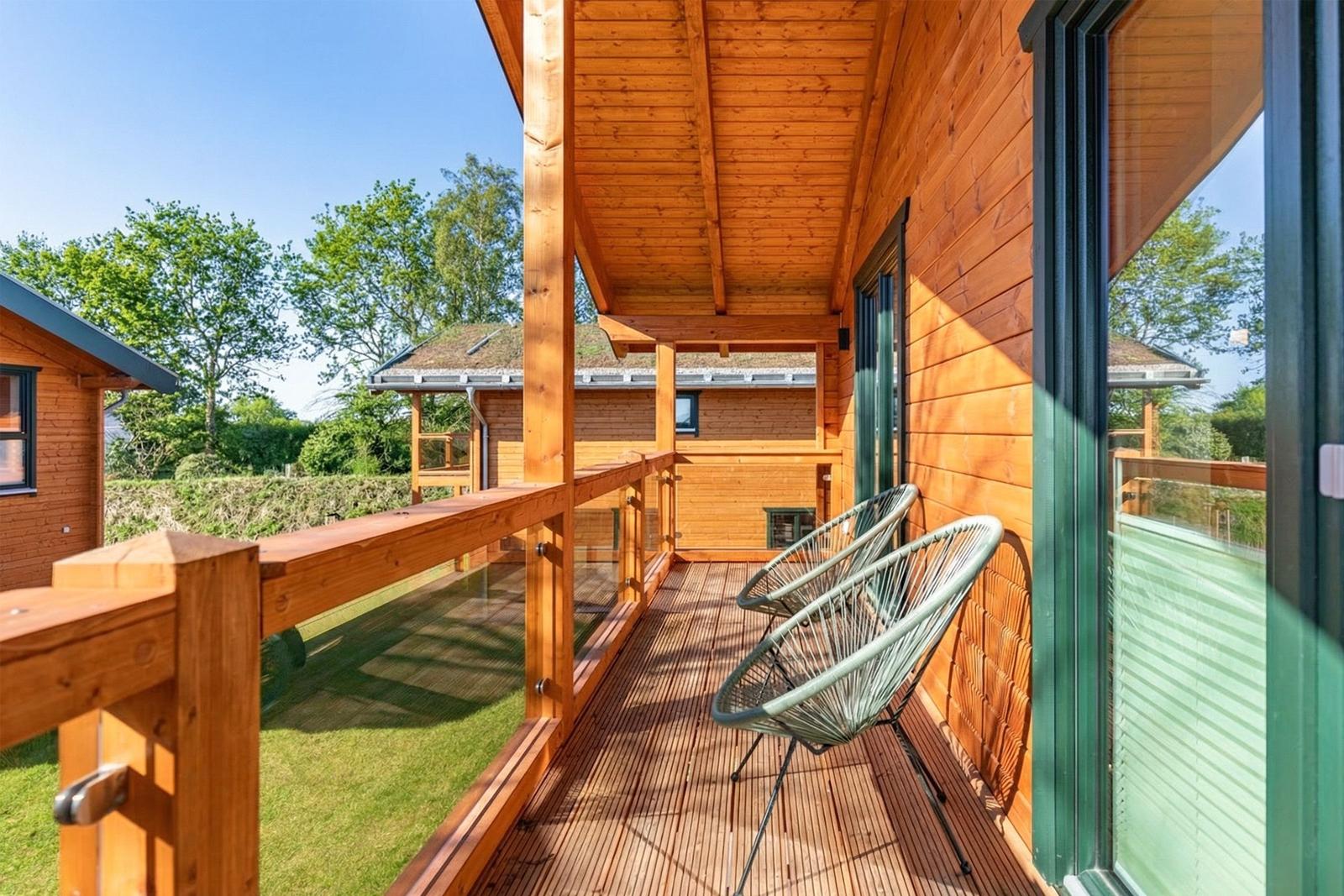 Holzveranda mit zwei grünen Sesseln und Blick auf Garten und Nachbarhäuser.