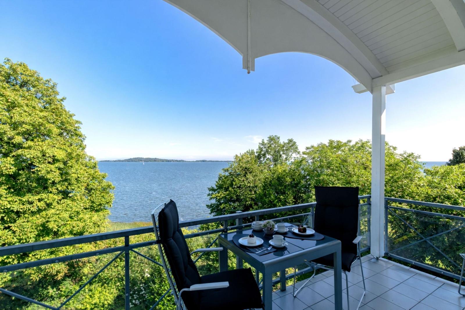 Terrasse mit Tisch und zwei Stühlen bietet Blick auf See und Bäume.