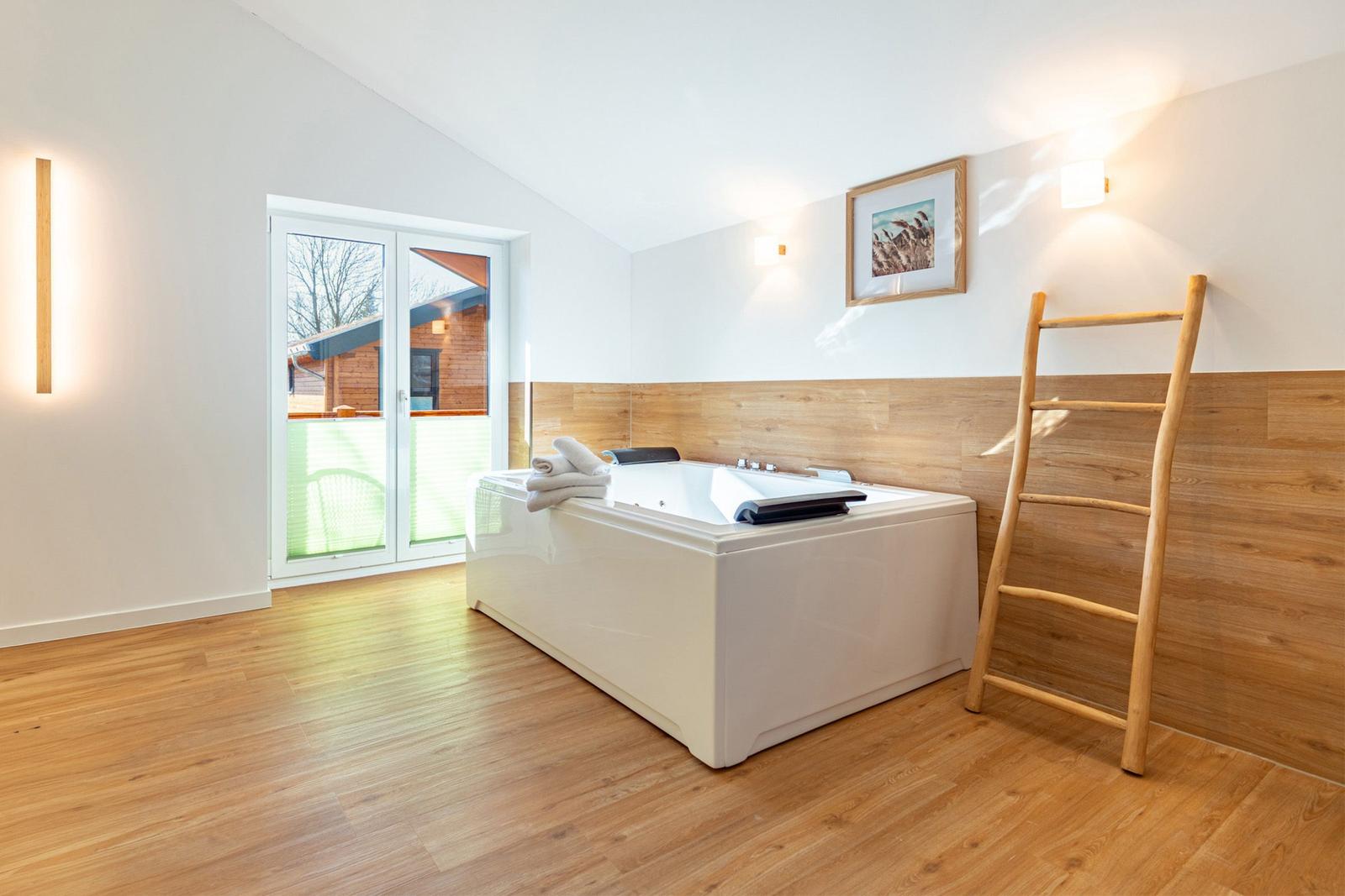 Bad mit Whirlpool, Holzfußboden und Fenster zum Balkon.