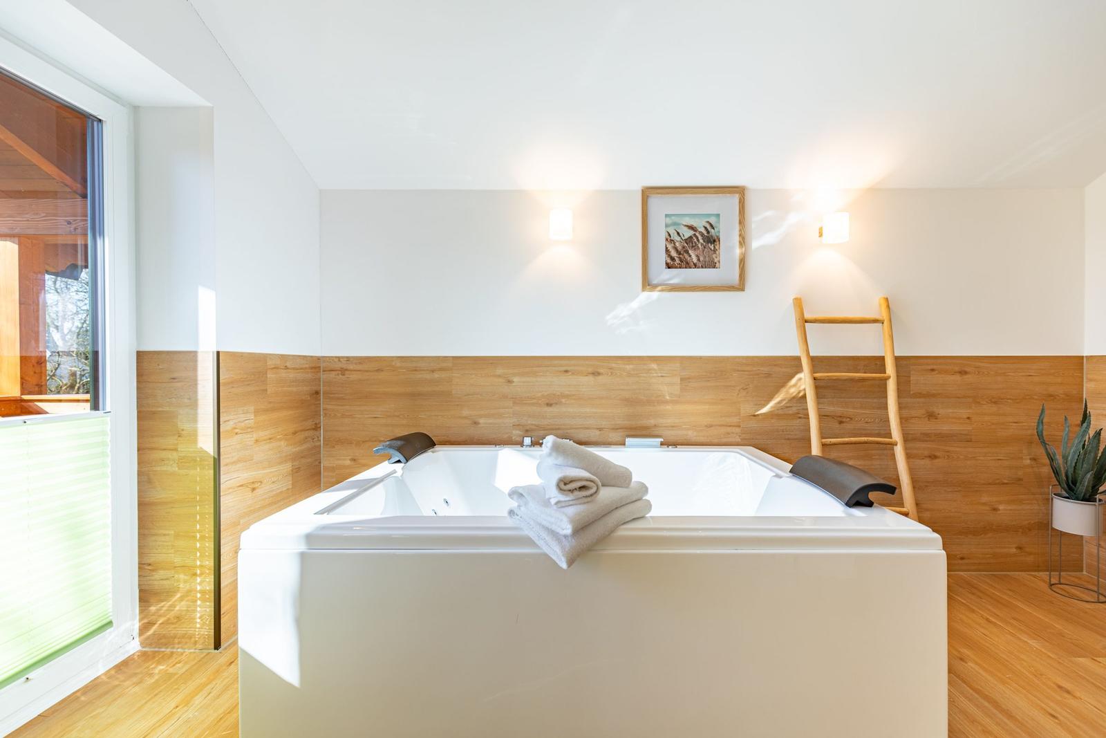 Whirlpool-Bad mit Holzwand und Fenster. Davor liegt ein weißer Handtuchstapel.