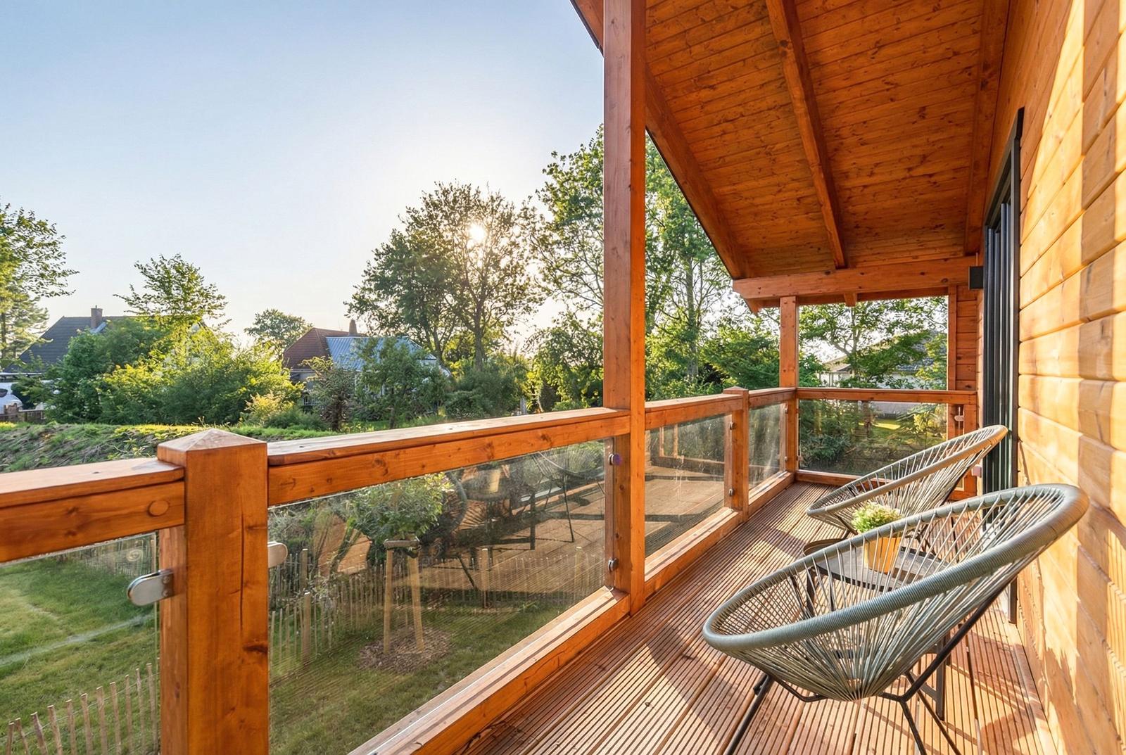 Terrasse mit Holzgeländer und Sitzgelegenheiten. Blick auf grüne Landschaft und Bäume.