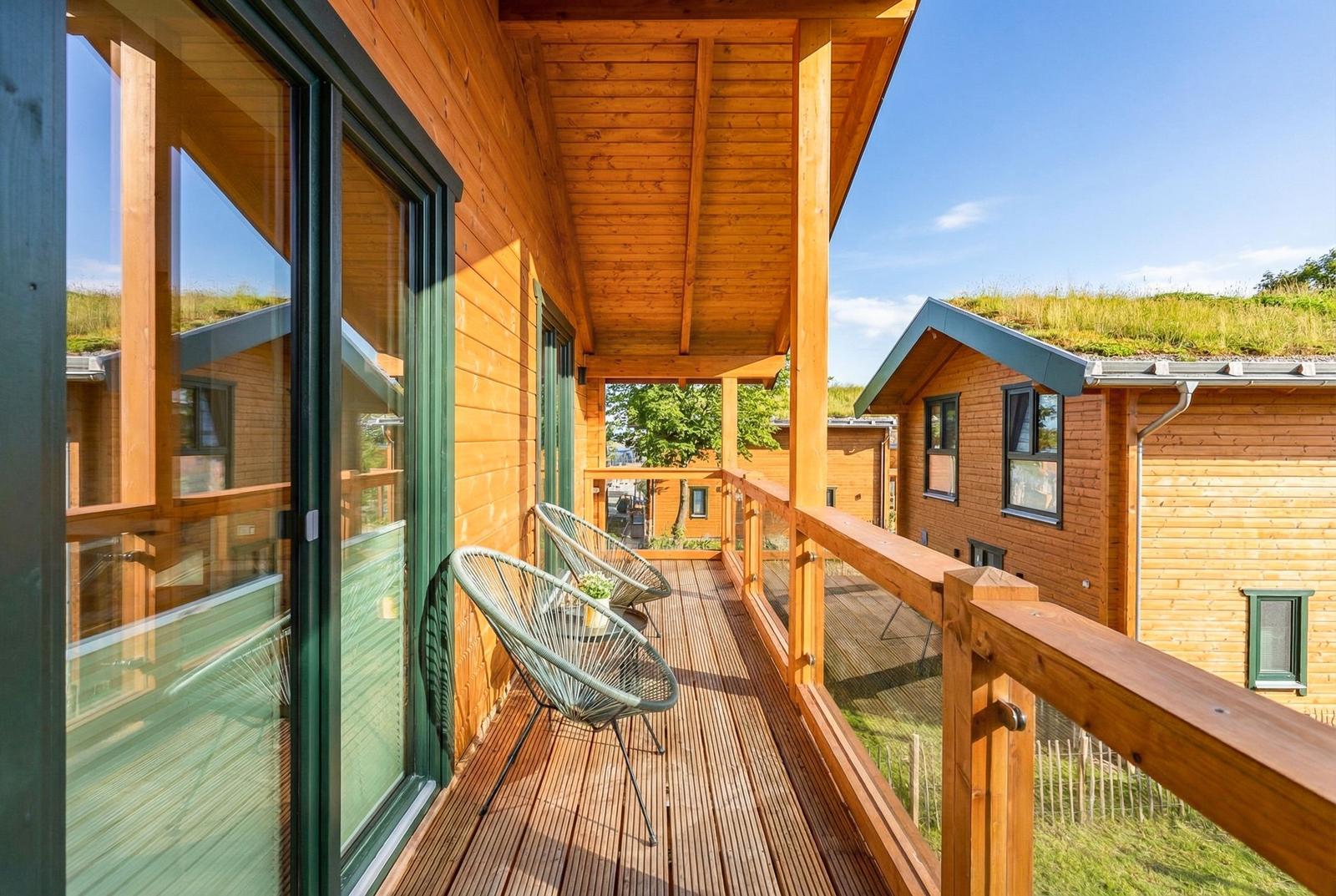 Holzveranda mit Stuhl und Tisch, Blick auf grünen Dachbereich und Nachbarhaus.
