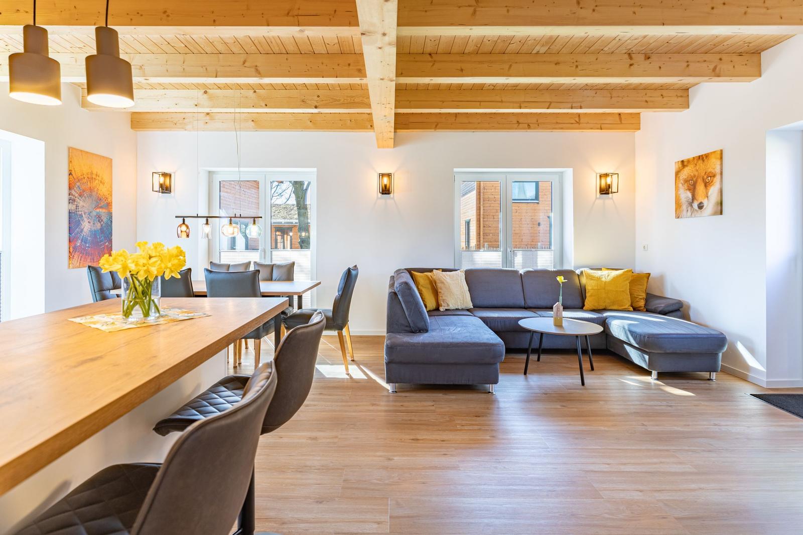 Wohn- und Essbereich mit Holzbalkendecke, grauem Sofa und Holzboden.