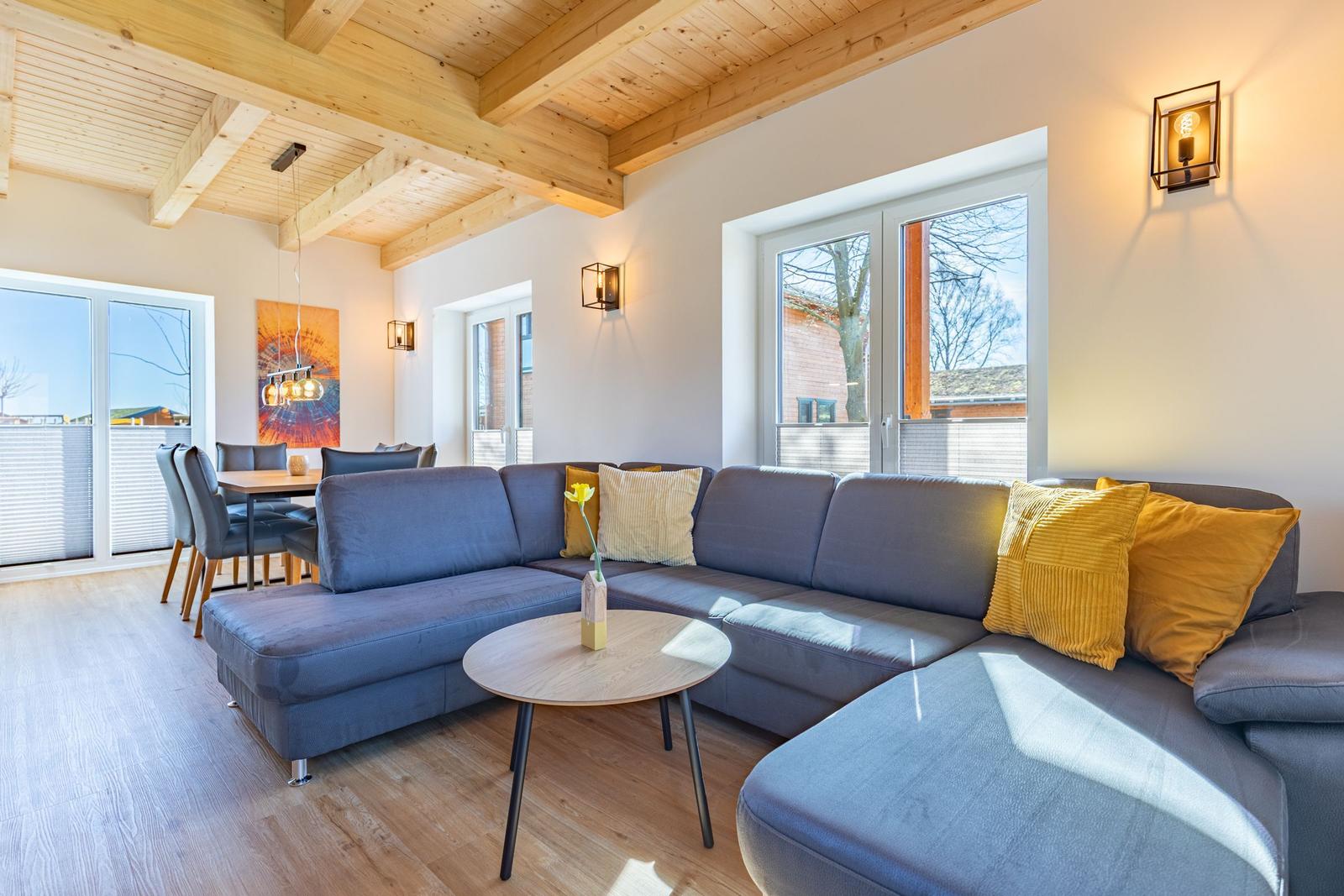 Ein Wohnzimmer mit grauem Sofa, gelben Kissen und Holzboden. An der Wand hängt ein Bild.