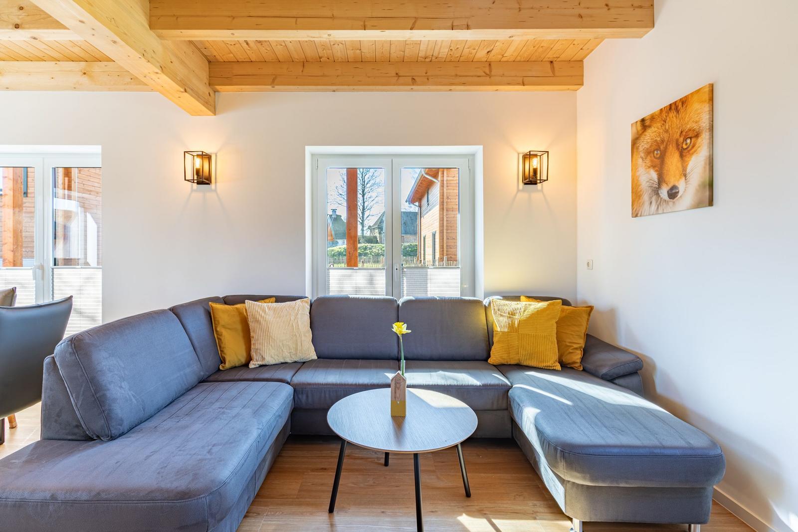 Ein Wohnzimmer mit grauem Sofa, gelben Kissen und Holzbalkendecke.
