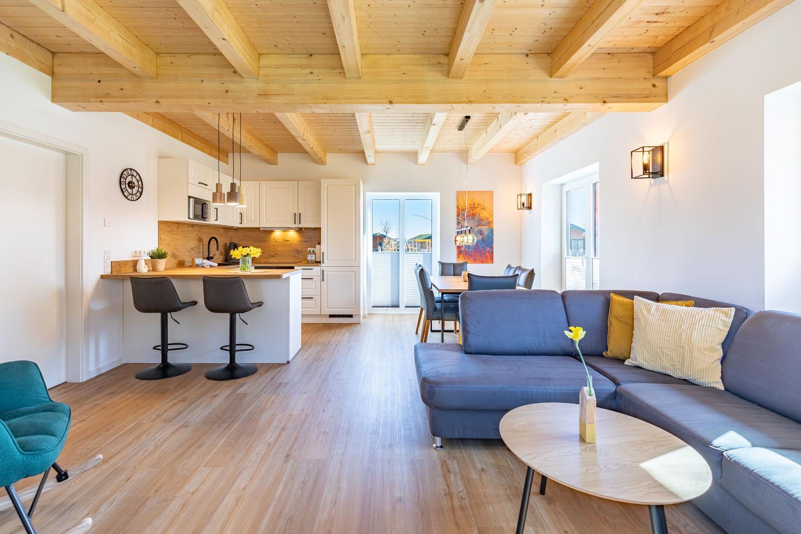 Wohnbereich mit Sofa, Esstisch und Küche unter Holzbalkendecke.