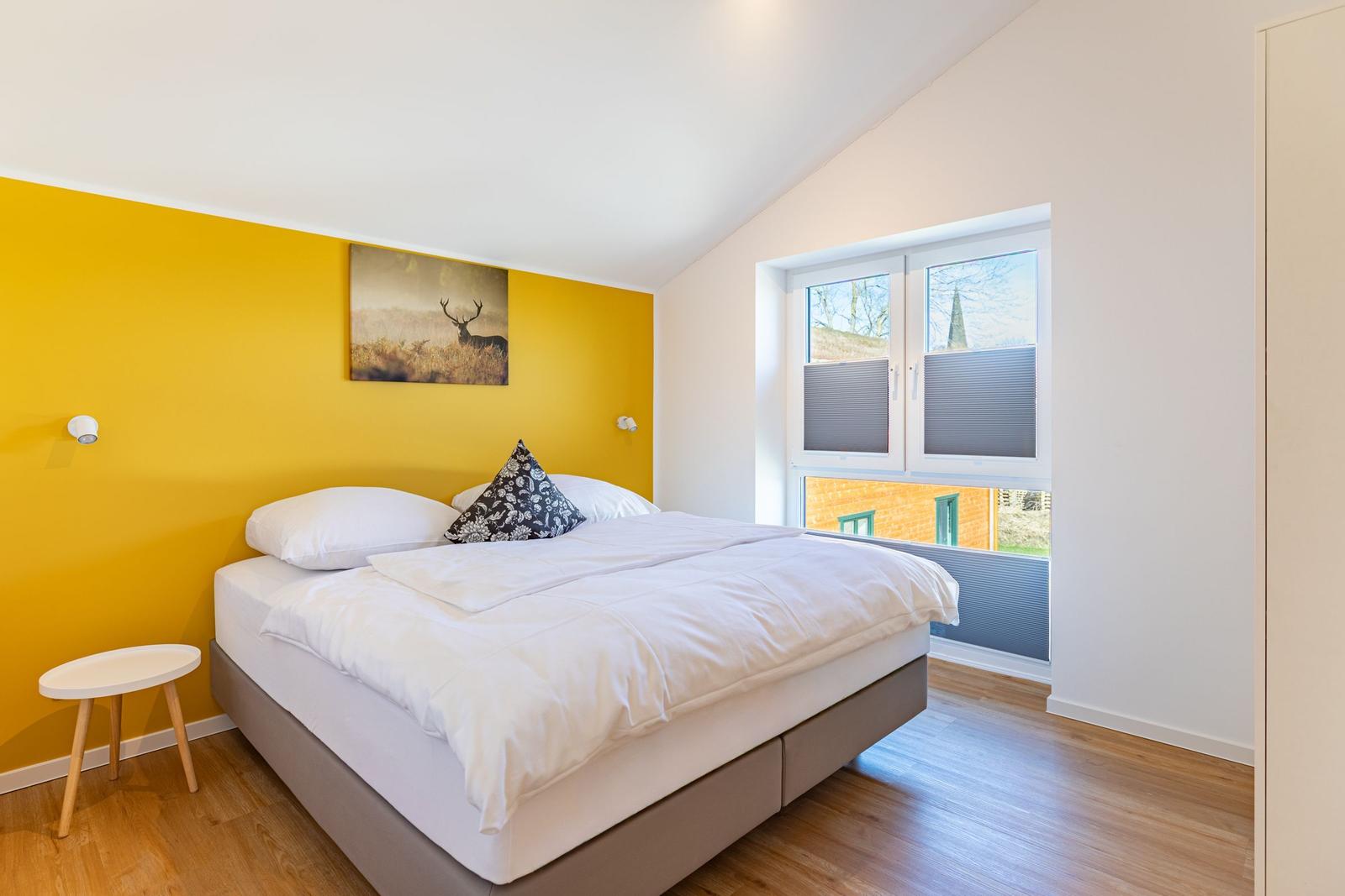 Schlafzimmer mit gelber Wand, Bett und Fenster mit Blick.