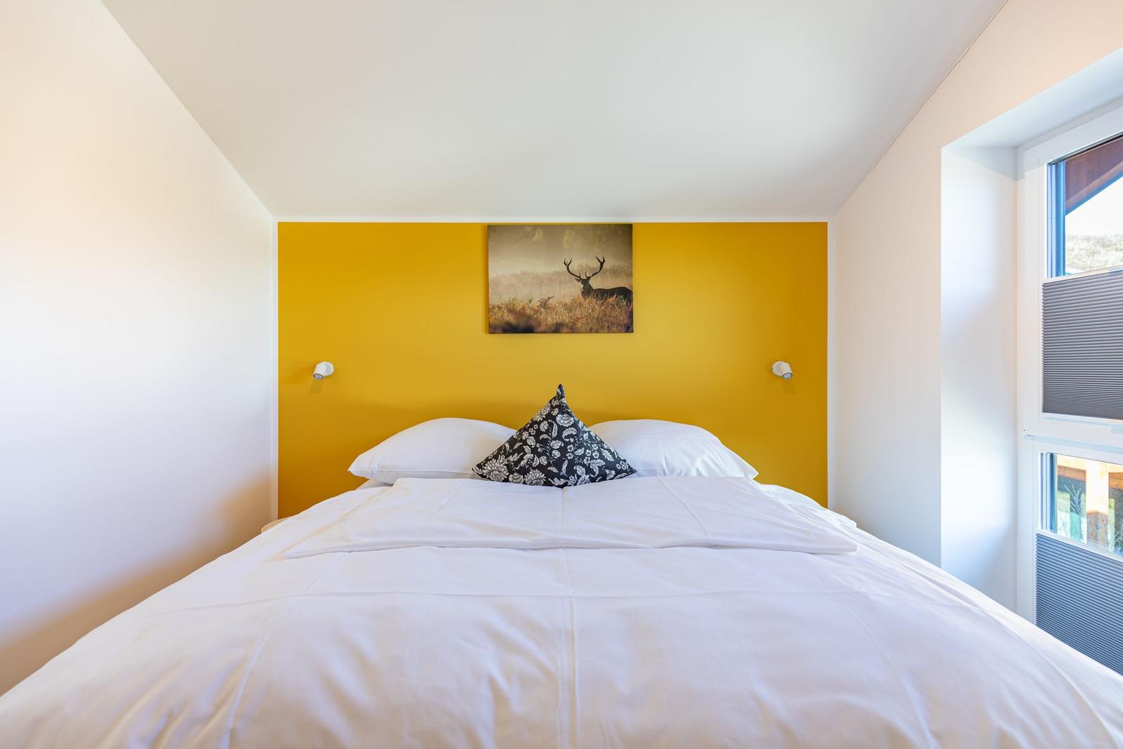 Schlafzimmer mit gelber Wand, Bett und Wandbild eines Hirsches.