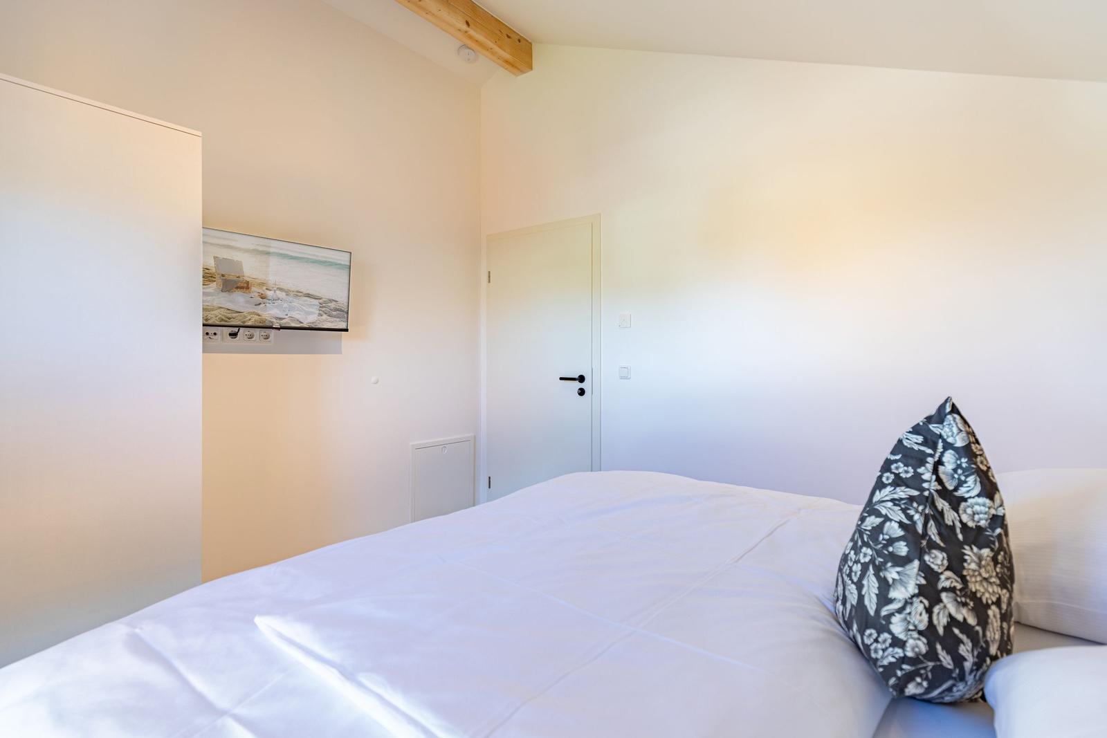 Schlafzimmer mit Bett, Kissen und Wandbild. Tür und Holzbalken sind sichtbar.