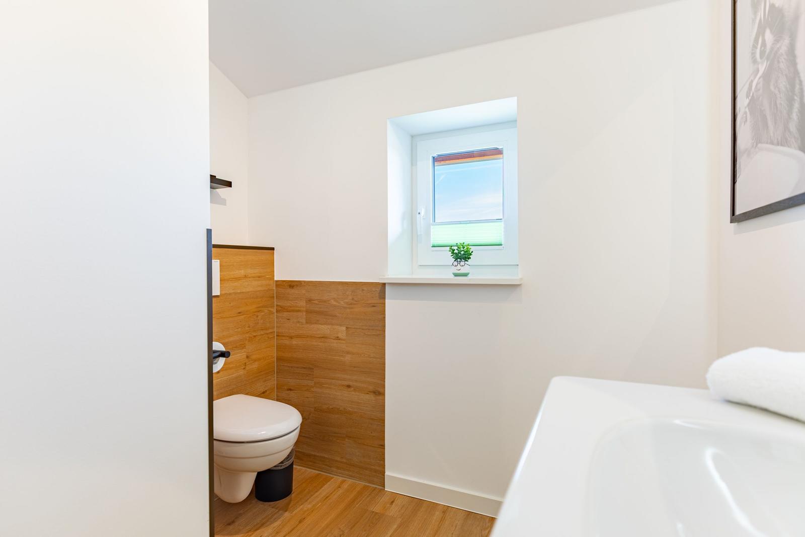 Bad mit Toilette, Fenster und Badewanne. Holzvertäfelung an der Wand.