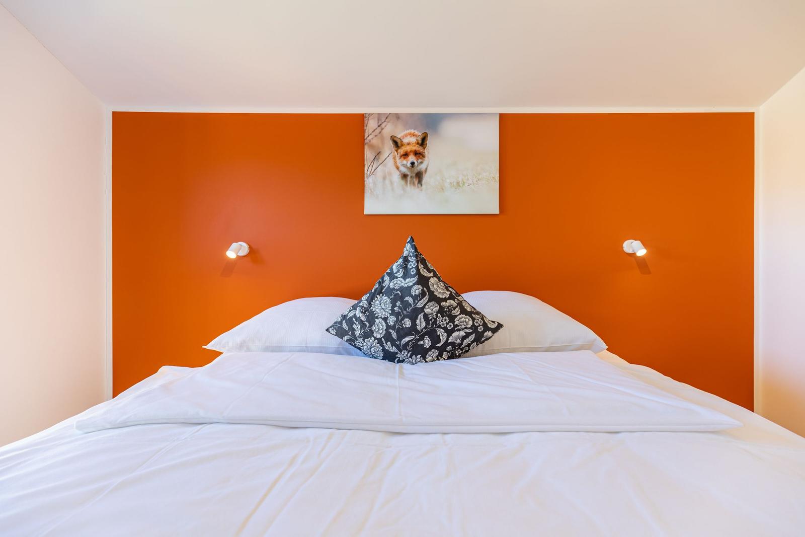 Schlafzimmer mit orangefarbener Wand, Bett mit weißen Laken und Kissen, Wandbild eines Fuchses.